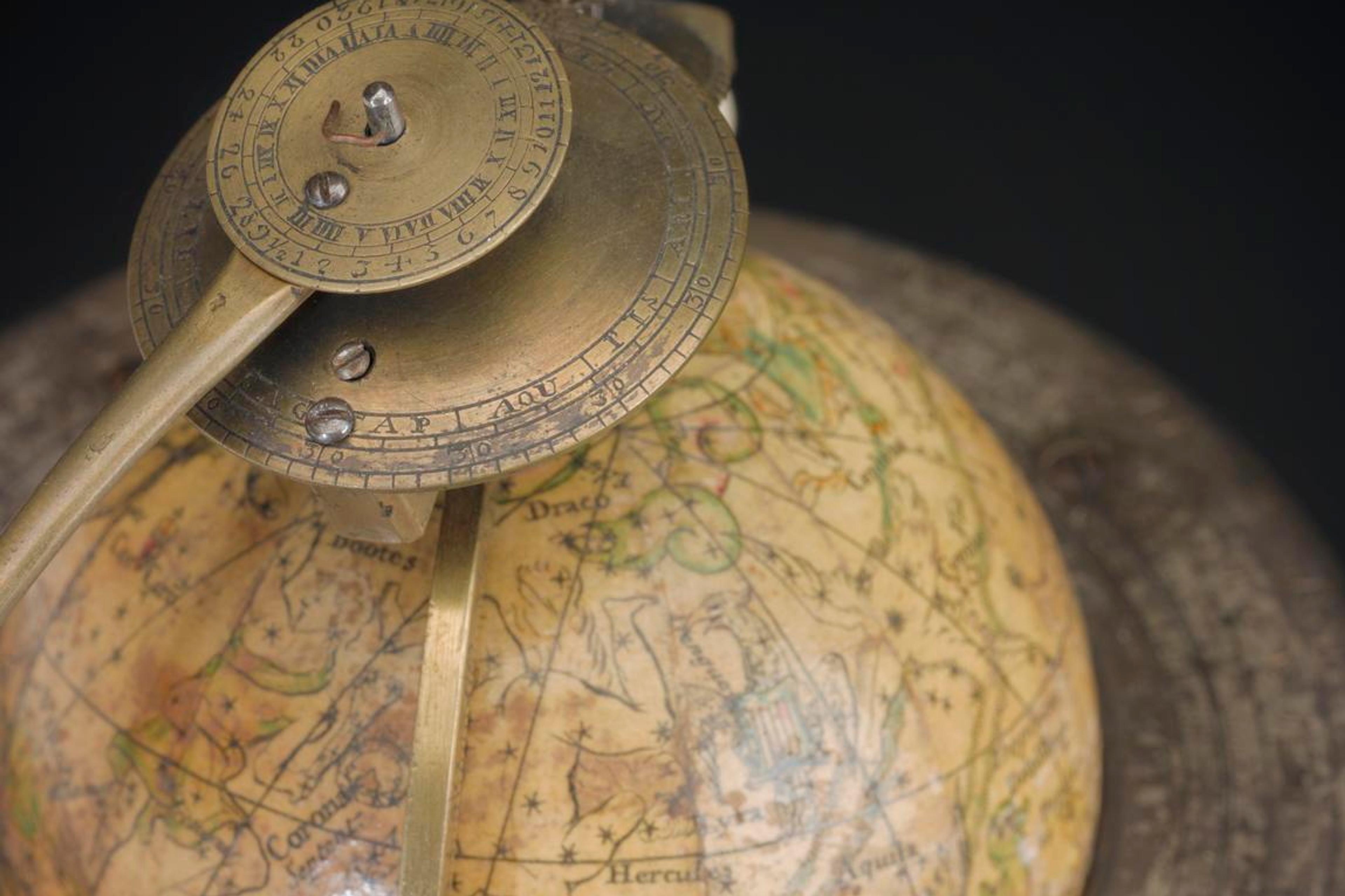 Photo of an antique celestial globe with brass armillary sphere detailing constellations on a decorative background.
