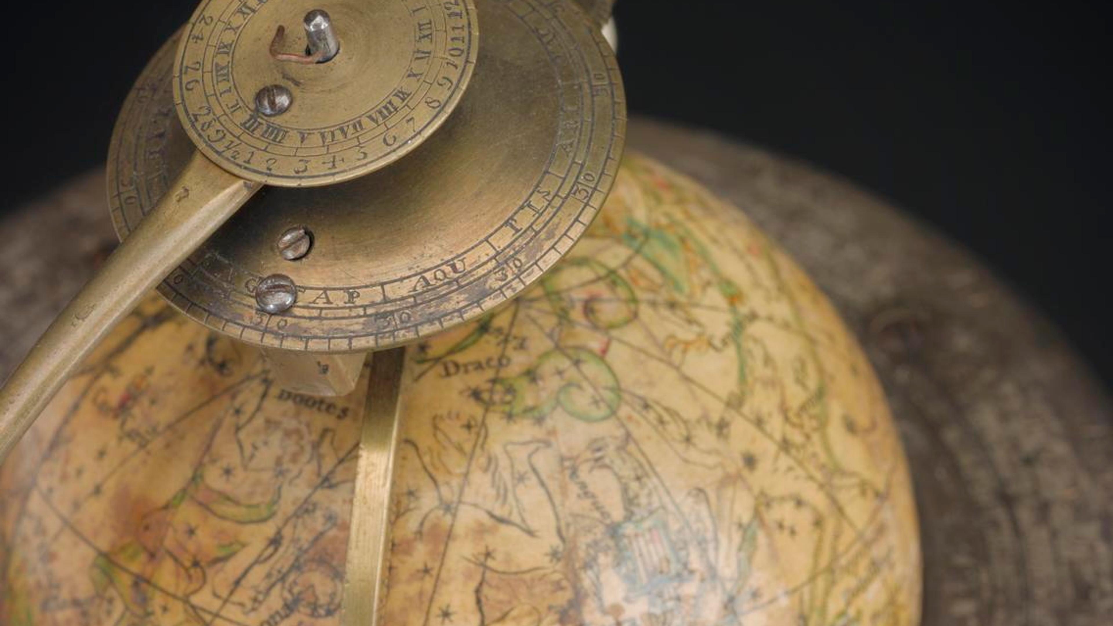 Photo of an antique celestial globe with brass armillary sphere detailing constellations on a decorative background.