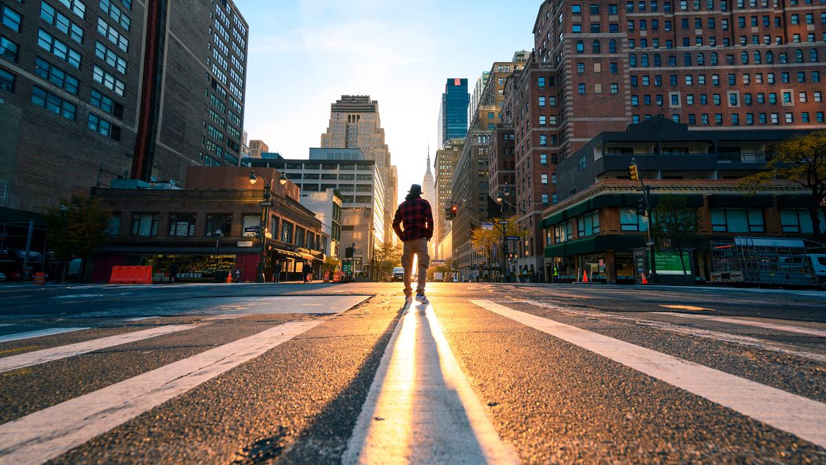 Photo of a person walking on an empty city street at sunrise, casting a long shadow amidst tall buildings.