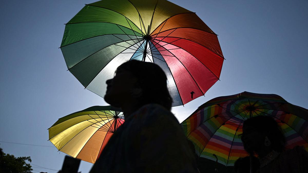 Silhouetted people under large vibrant, colourful umbrellas against a clear blue sky.