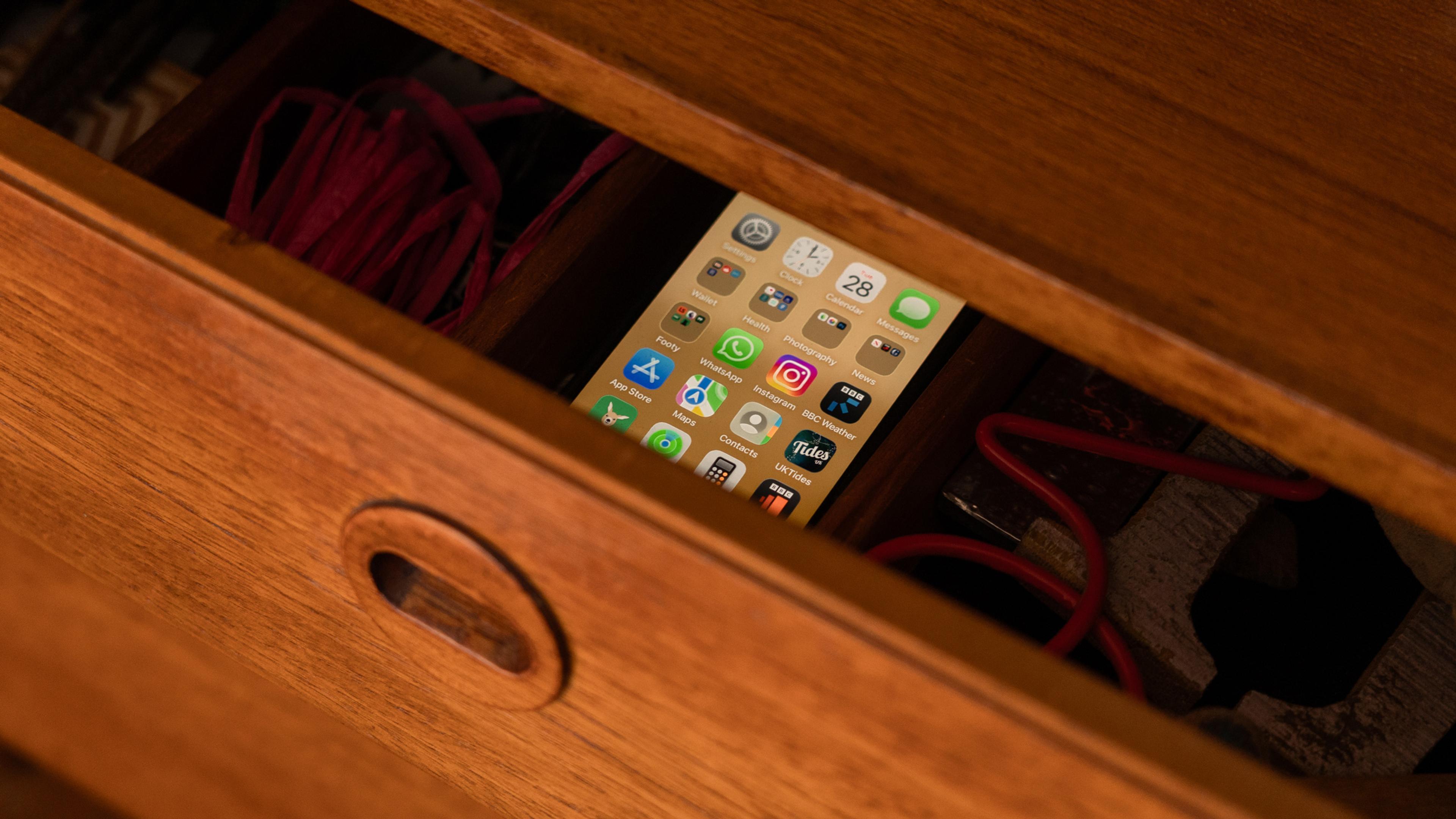 A smartphone with app icons visible inside an open wooden drawer with red cables partially visible.