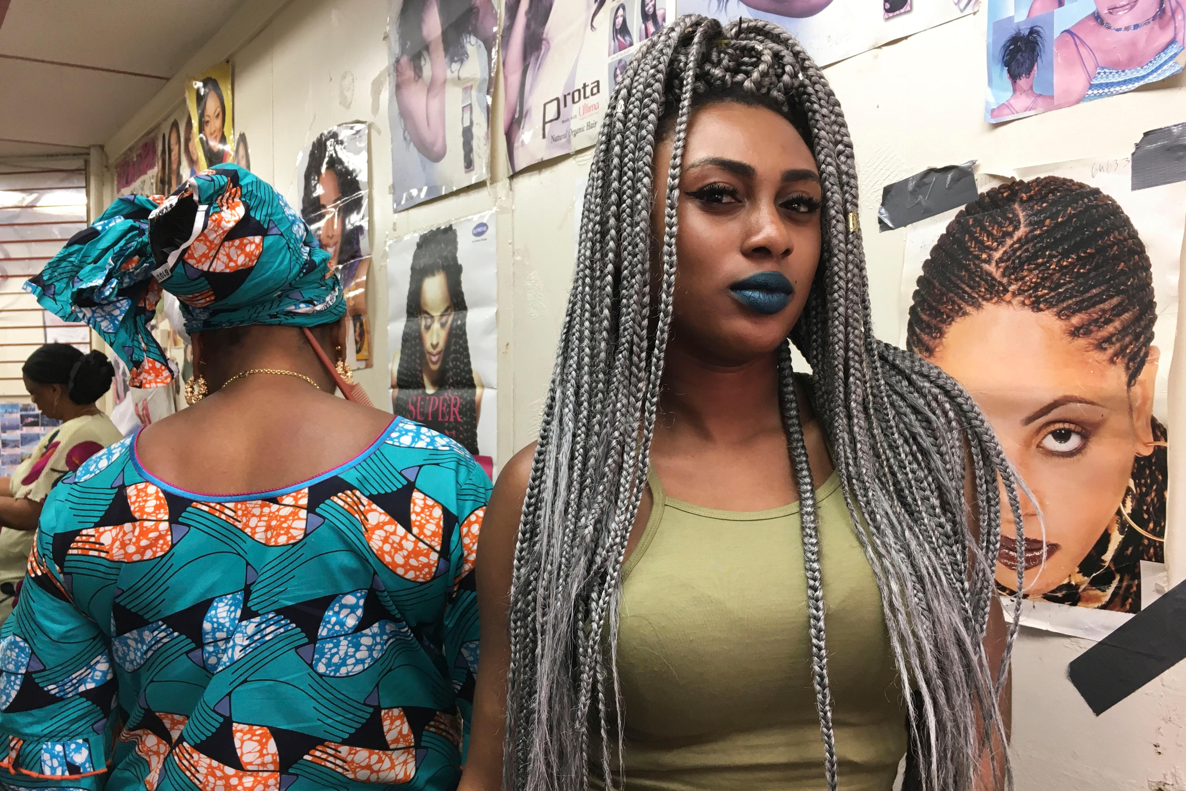 Photo of two women in a hair salon, one with grey braids in a green top, the other in a colourful patterned outfit.