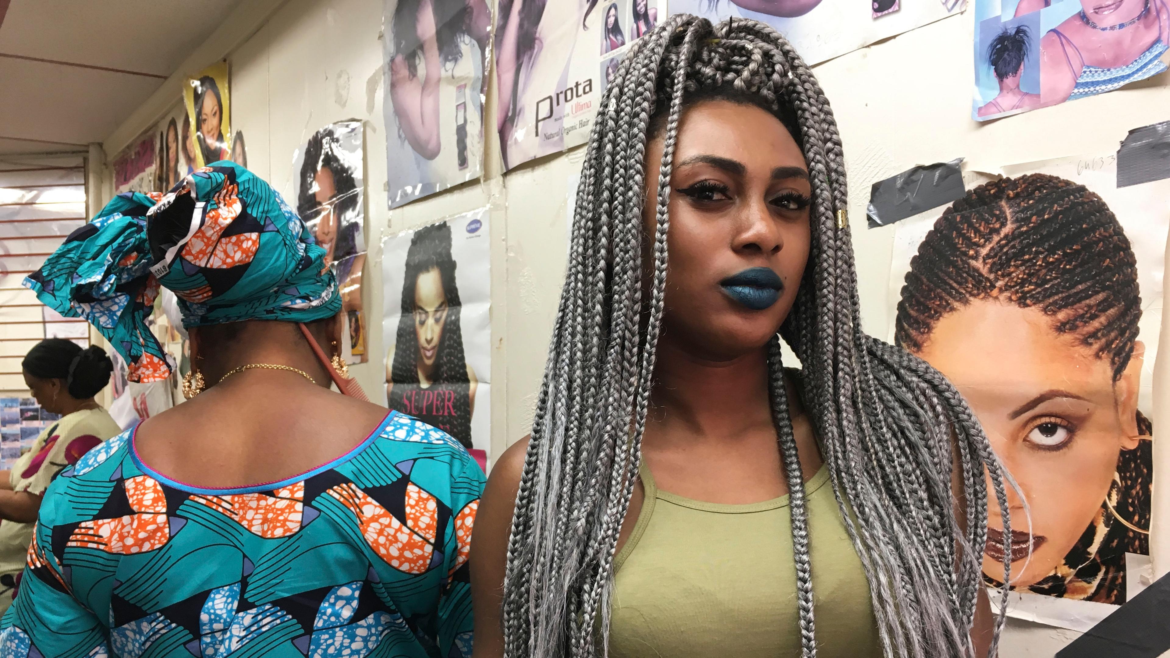 Photo of two women in a hair salon, one with grey braids in a green top, the other in a colourful patterned outfit.