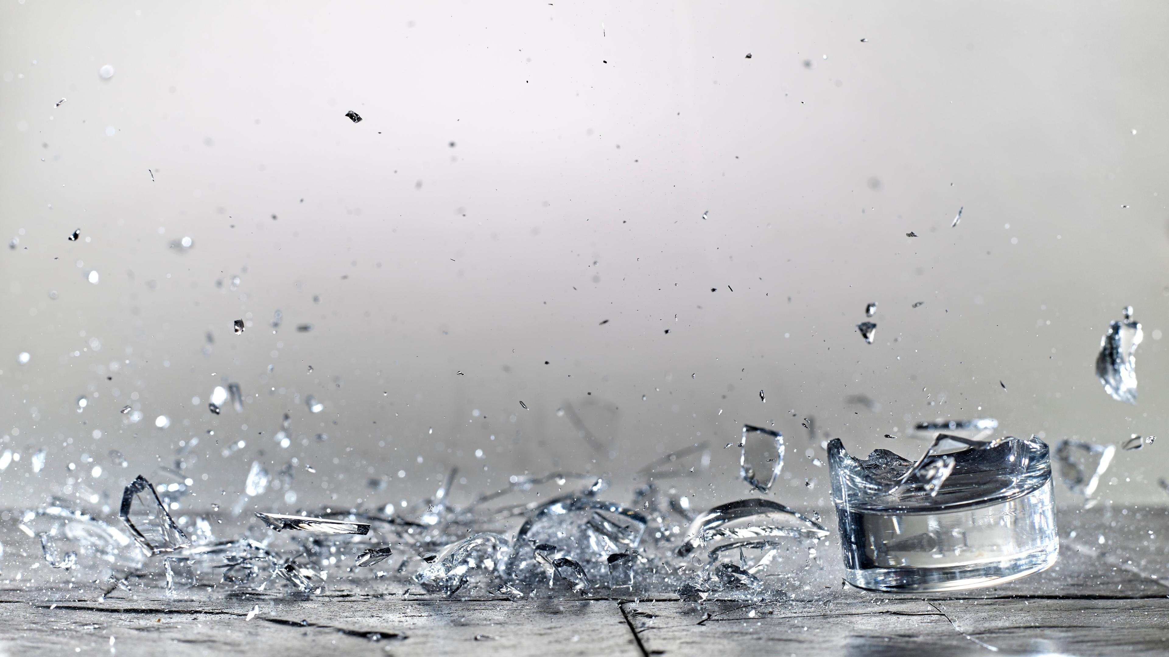 Photo of a glass shattering on a grey surface with shards scattered mid-air and on the ground.