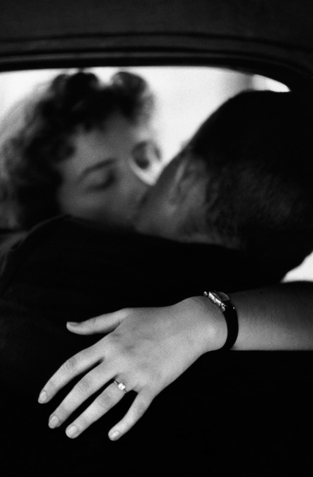 Black and white photo of a couple kissing, with focus on a woman’s hand wearing a ring and watch.