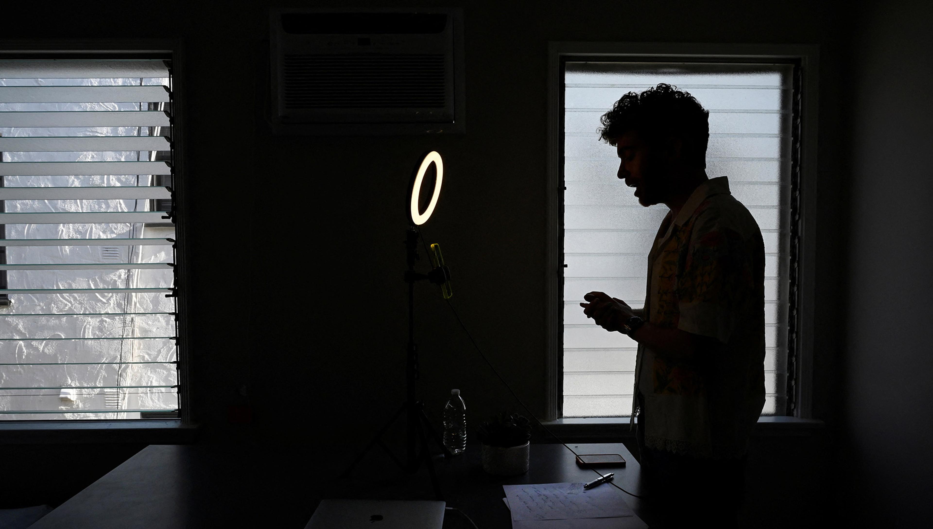 A man is silhouetted presenting to a video camera and lit by a ring light