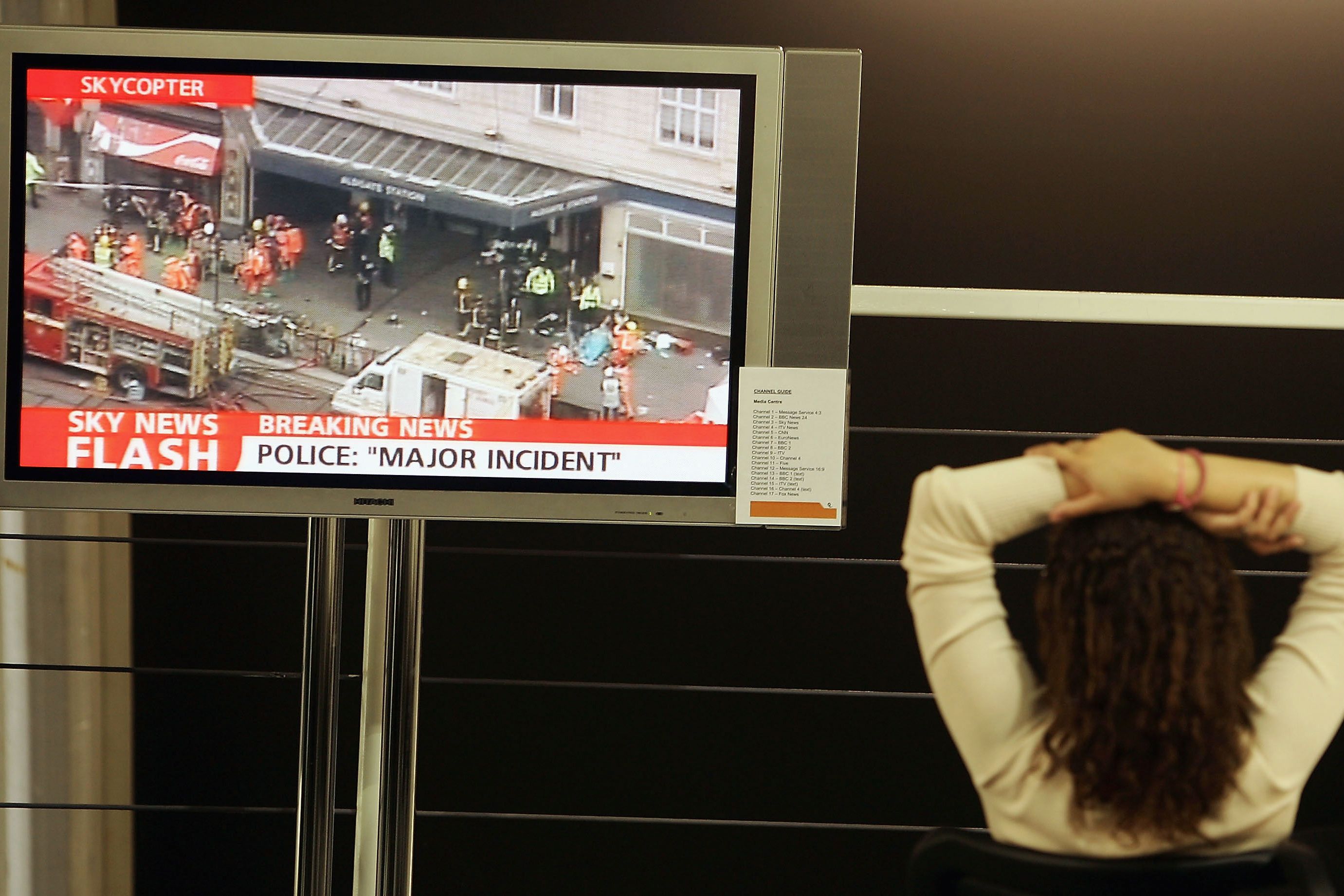 Woman watching TV screen showing breaking news about a major incident at a station, emergency services on site. Photo.