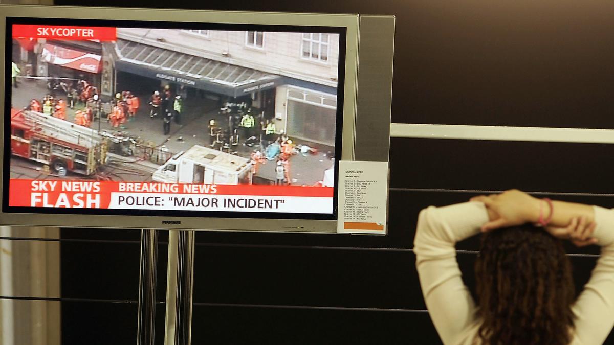 Woman watching TV screen showing breaking news about a major incident at a station, emergency services on site. Photo.