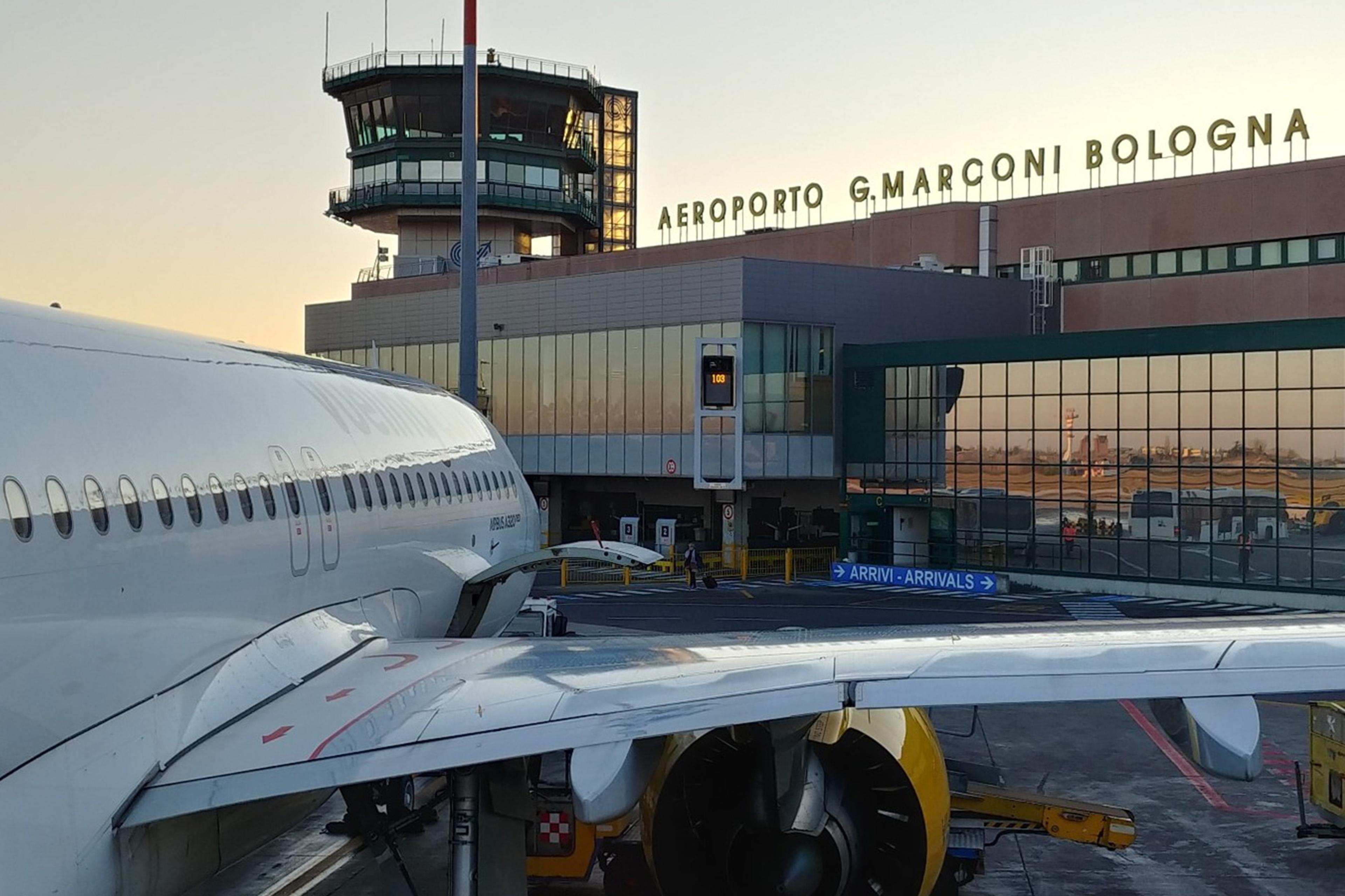 Photo of an aeroplane parked at Bologna Airport with the terminal and control tower in the background.
