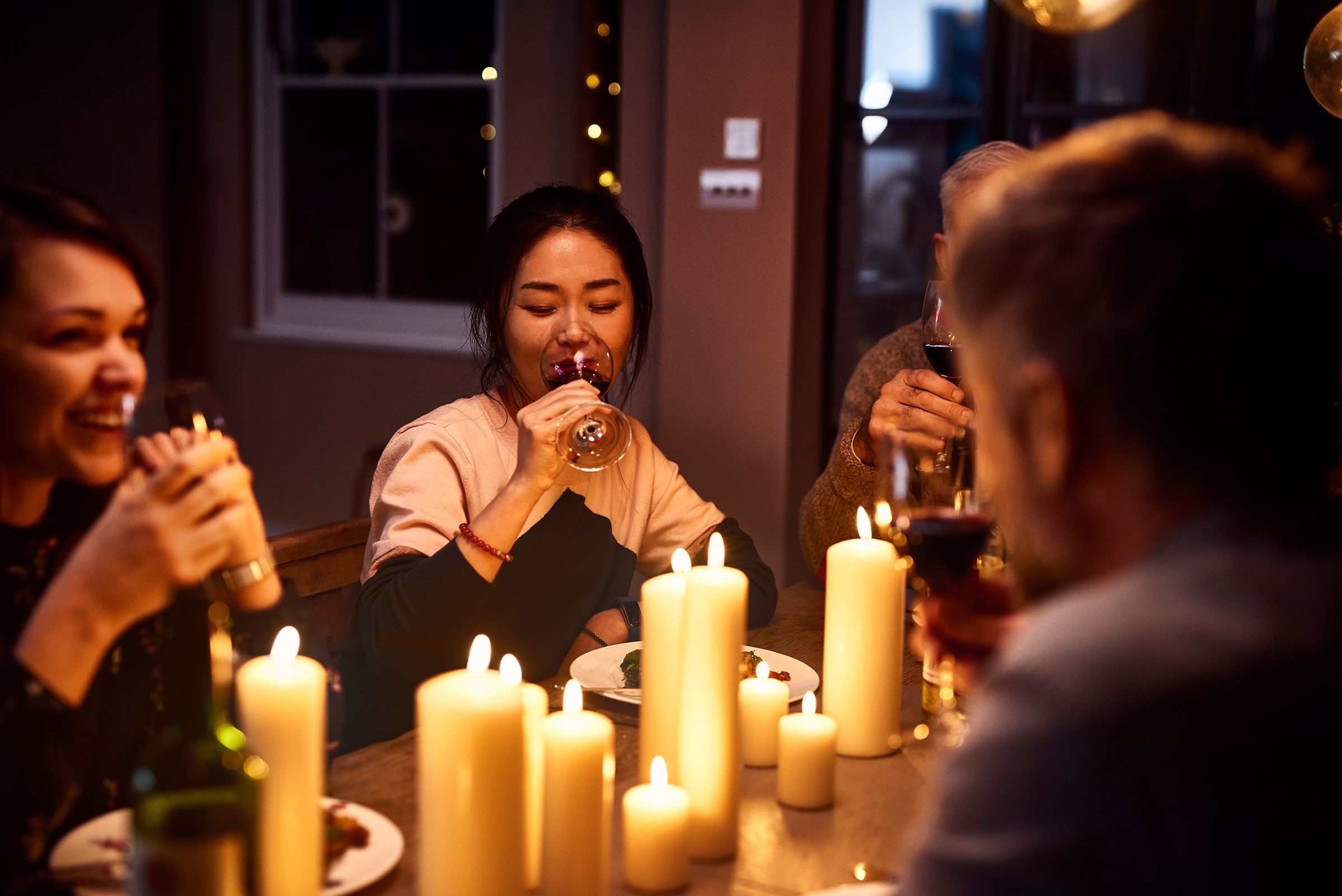 Friends enjoying a candlelit dinner, drinking wine and smiling warmly around a table.