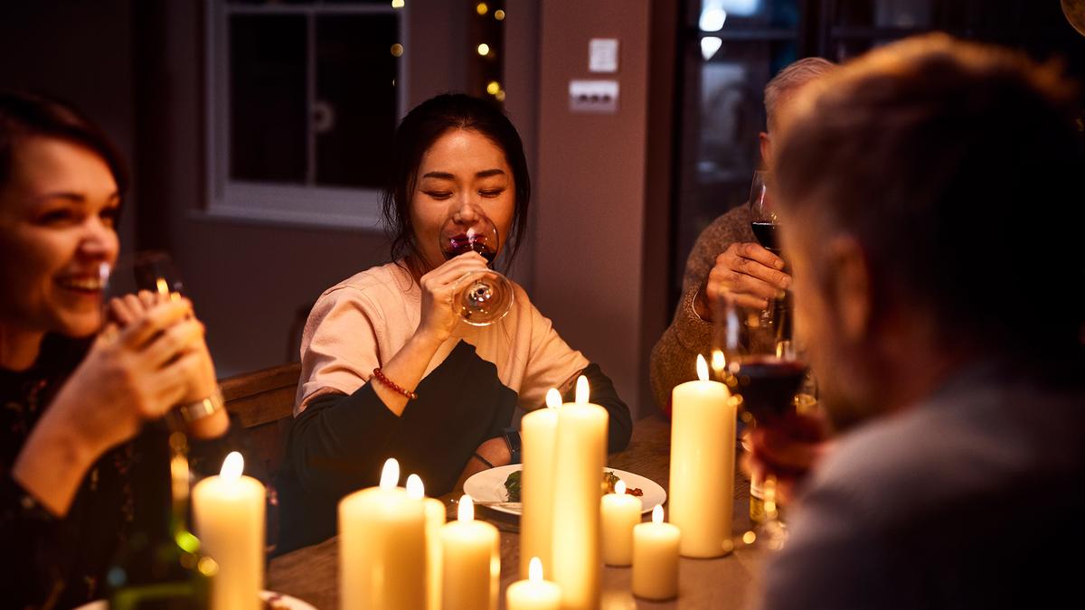 Friends enjoying a candlelit dinner, drinking wine and smiling warmly around a table.