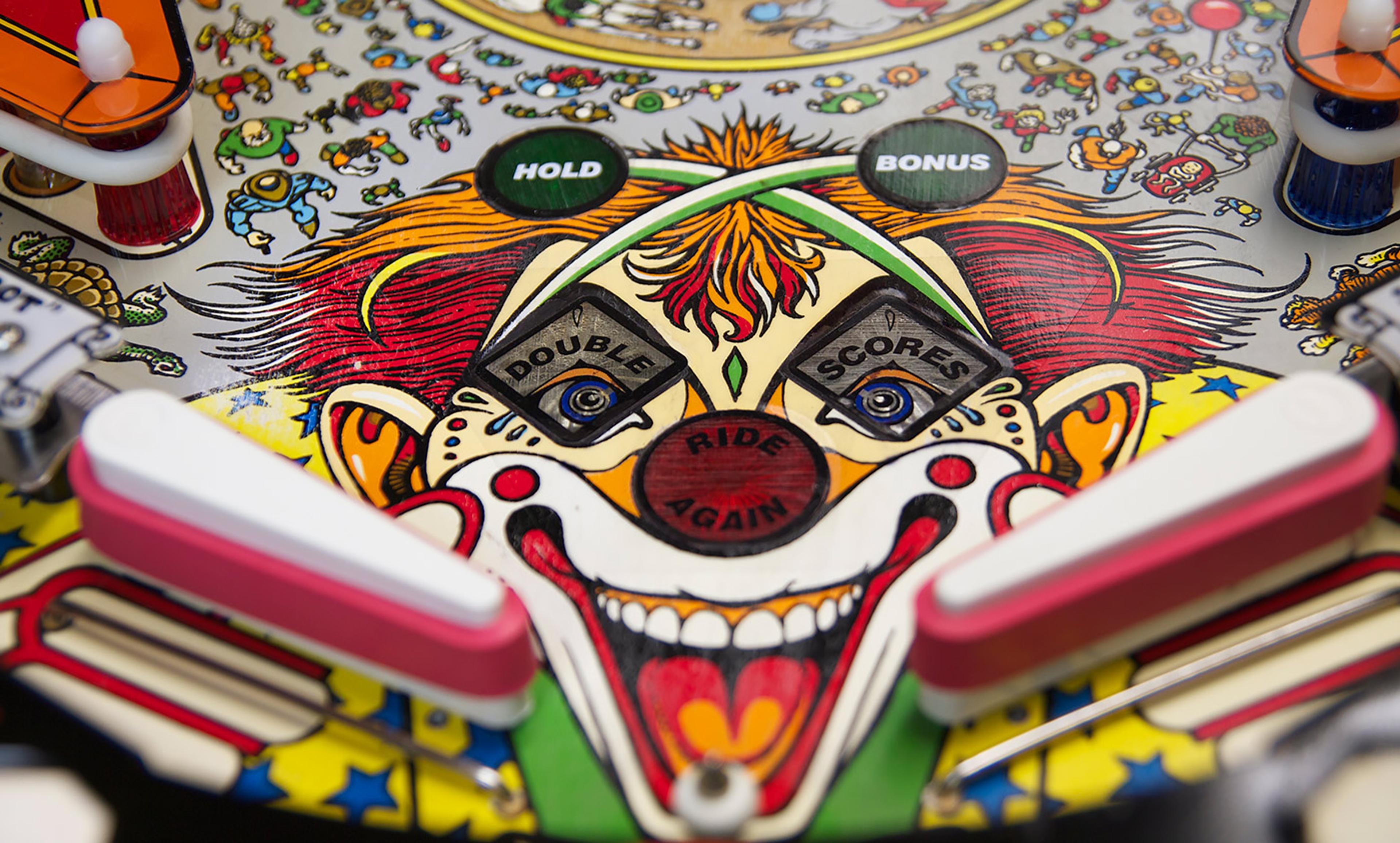 Close-up photo of a colourful vintage pinball machine featuring a clown face with flippers and various game elements.