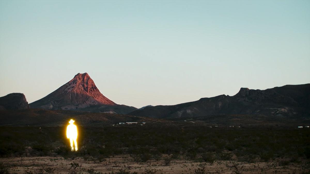 Photo of a glowing figure in a desert landscape with a mountain in the background under a clear sky.