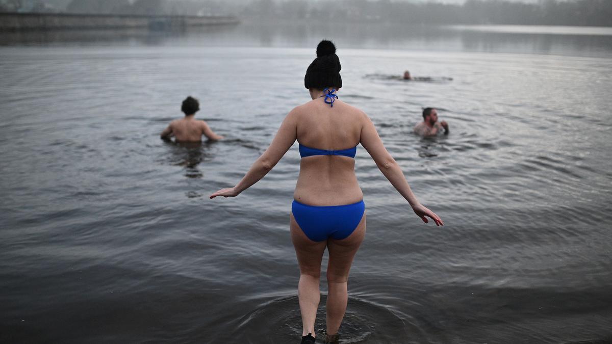 Photo of people swimming in a misty lake, with a person in a blue bikini entering the water in the foreground.