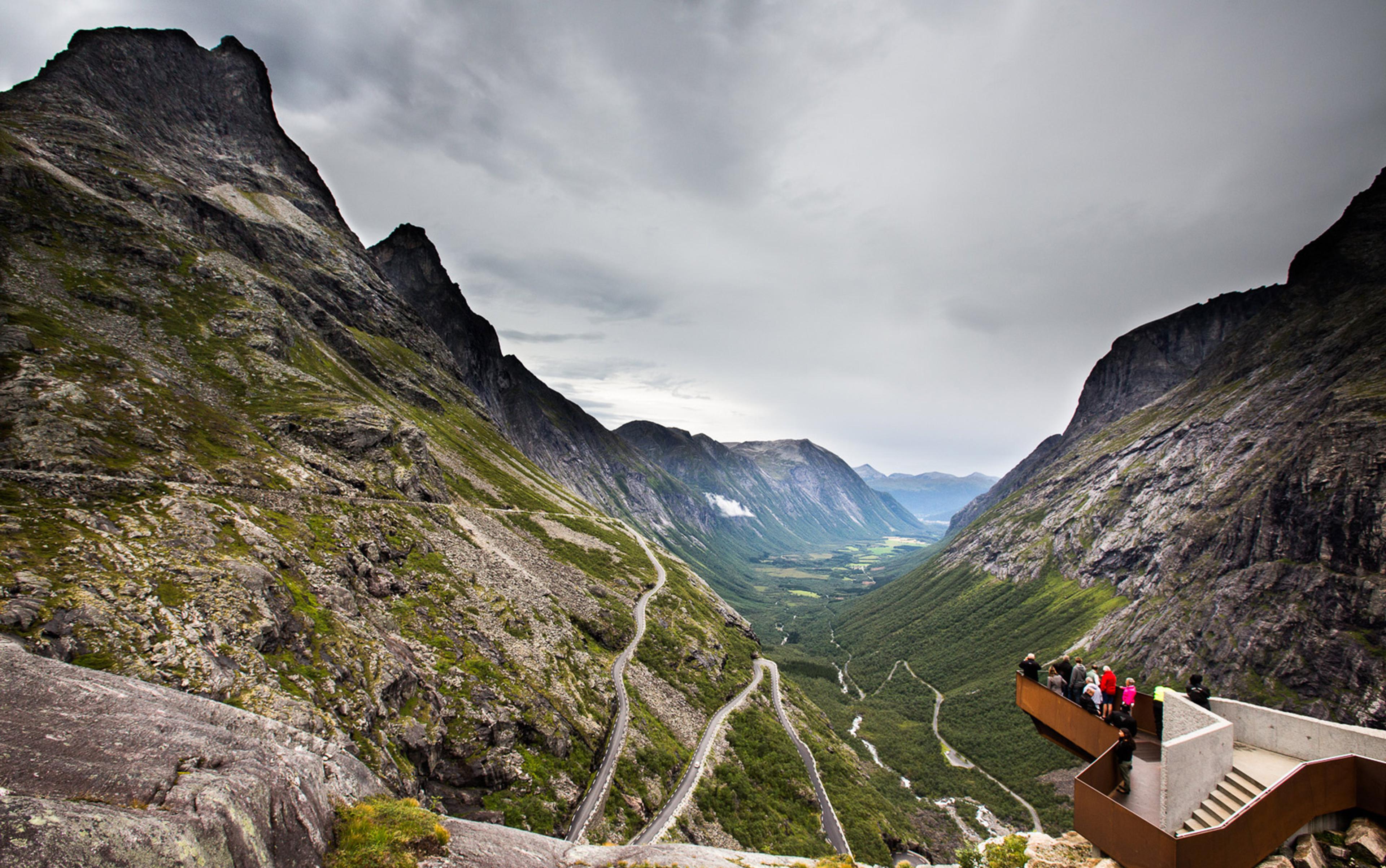 A scenic mountain valley with a winding road and a viewpoint platform where people are observing the landscape.