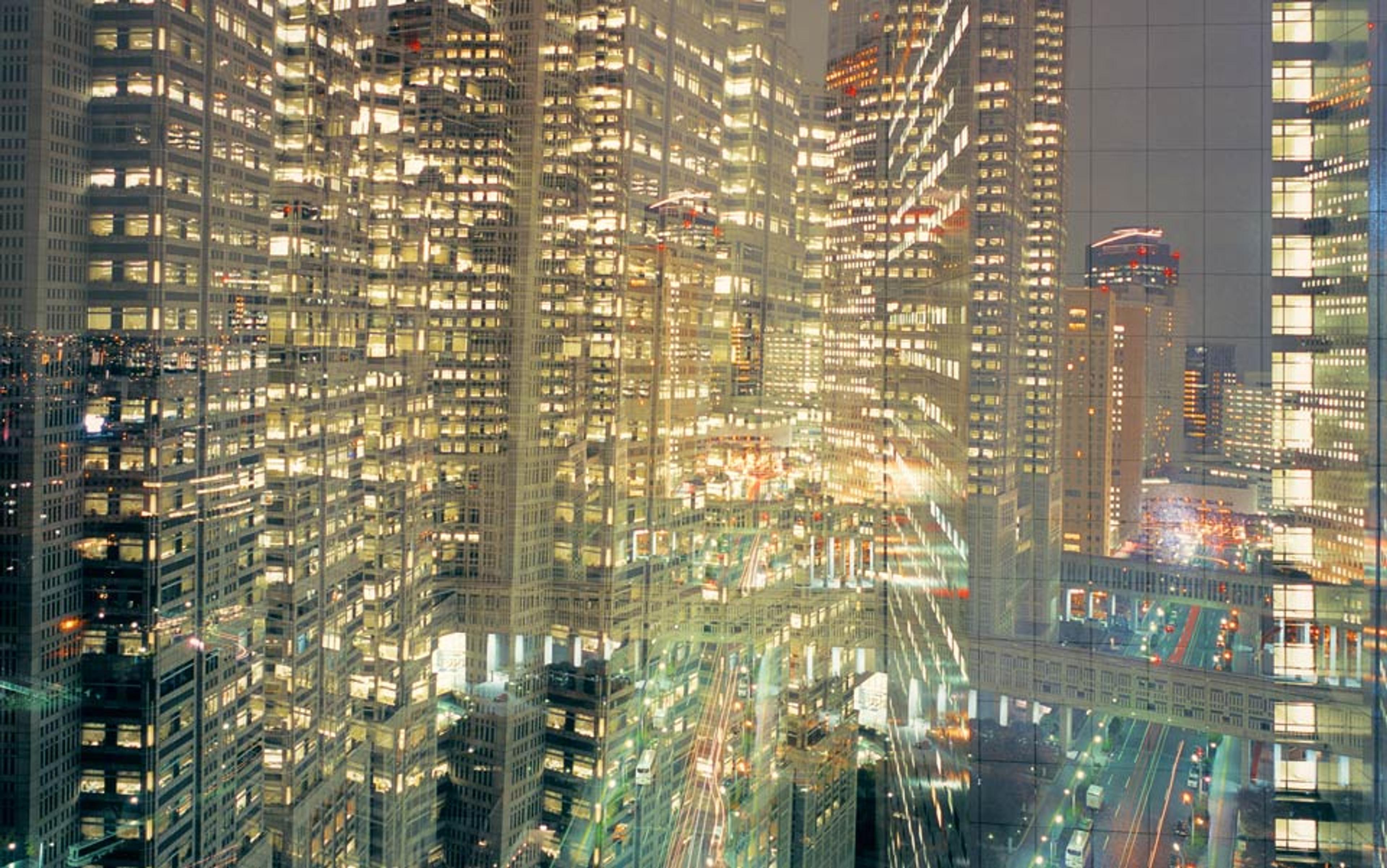 A cityscape at night with buildings illuminated, featuring reflections and light trails, creating a layered, abstract effect.