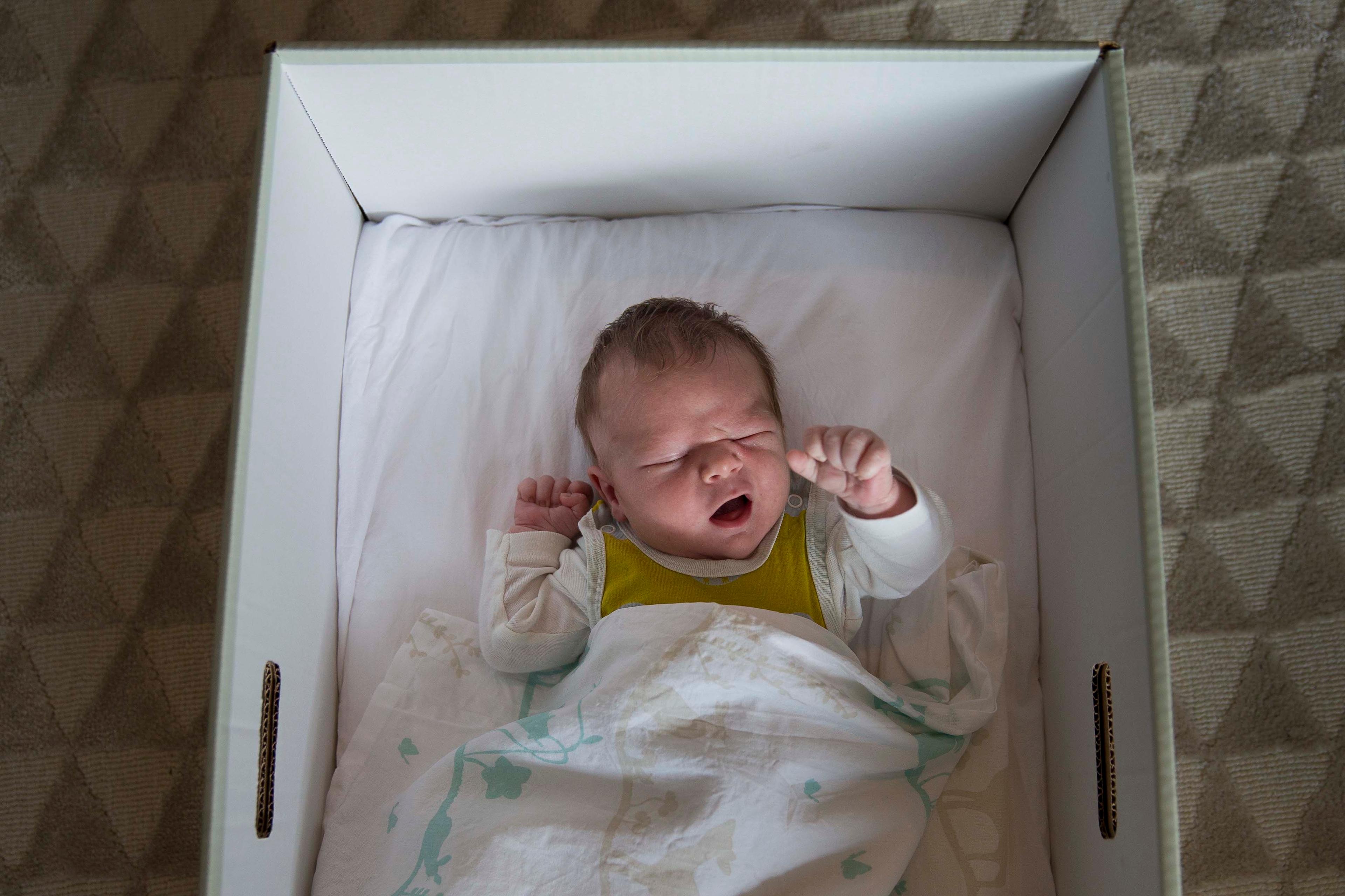 Photo of a newborn baby sleeping in a white box with a blanket on a patterned carpet background.