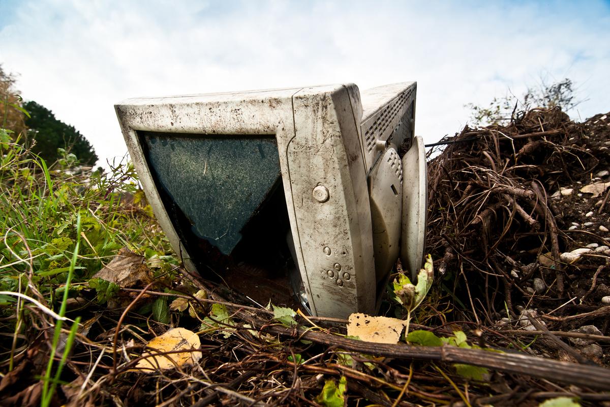 Photo of an old computer monitor discarded in nature, surrounded by grass and twigs under a cloudy sky.