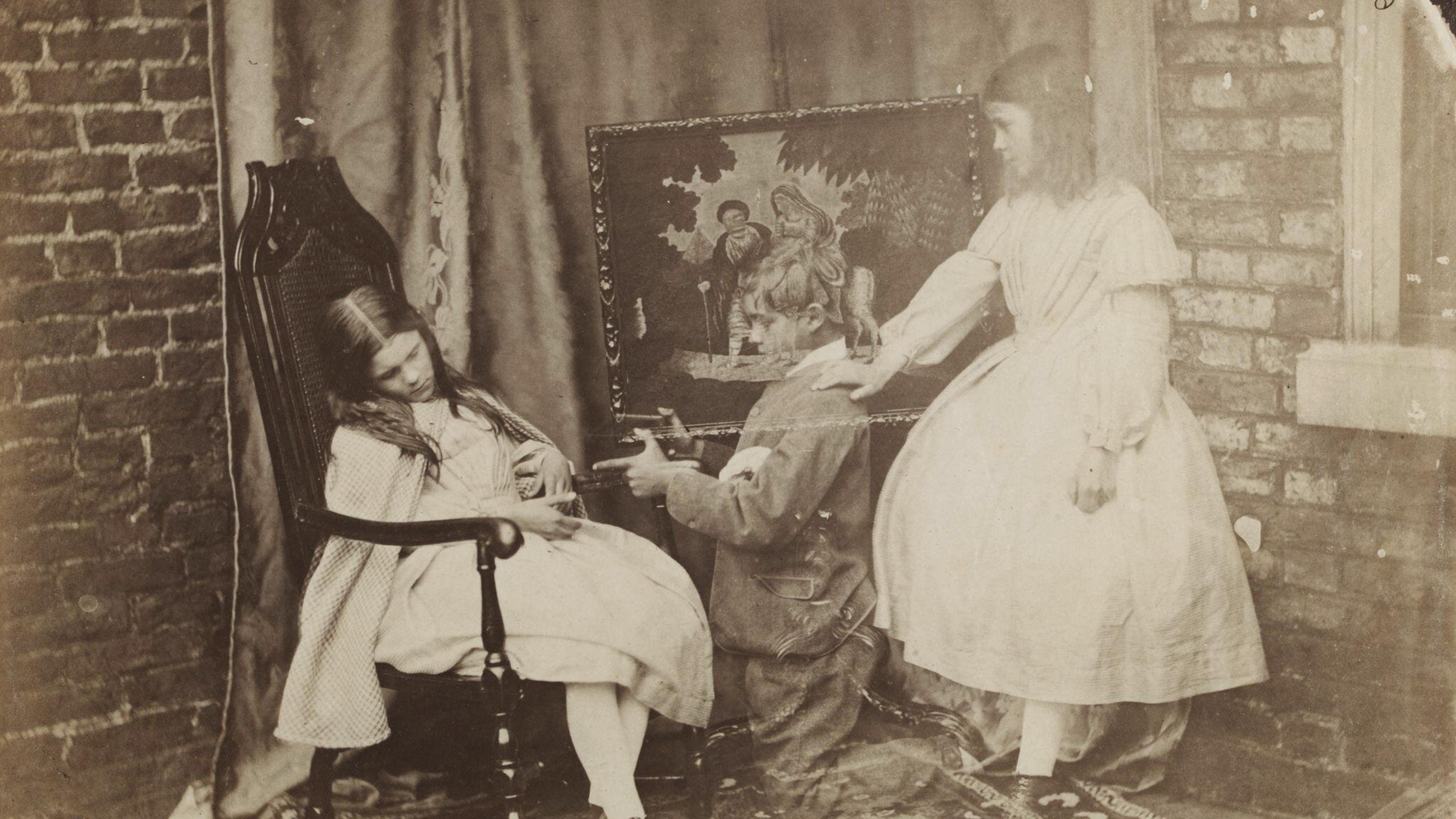 Old photograph of a girl sleeping in a chair, a ghostly boy kneeling before her, and a ghostly girl standing by a wall with a religious tapestry.