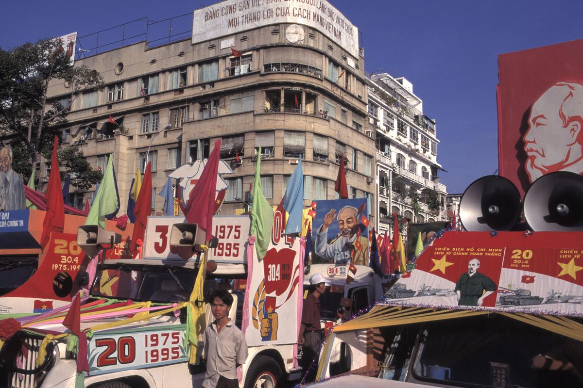 A vibrant street scene with decorated vehicles, colourful flags and banners in front of a large urban building.