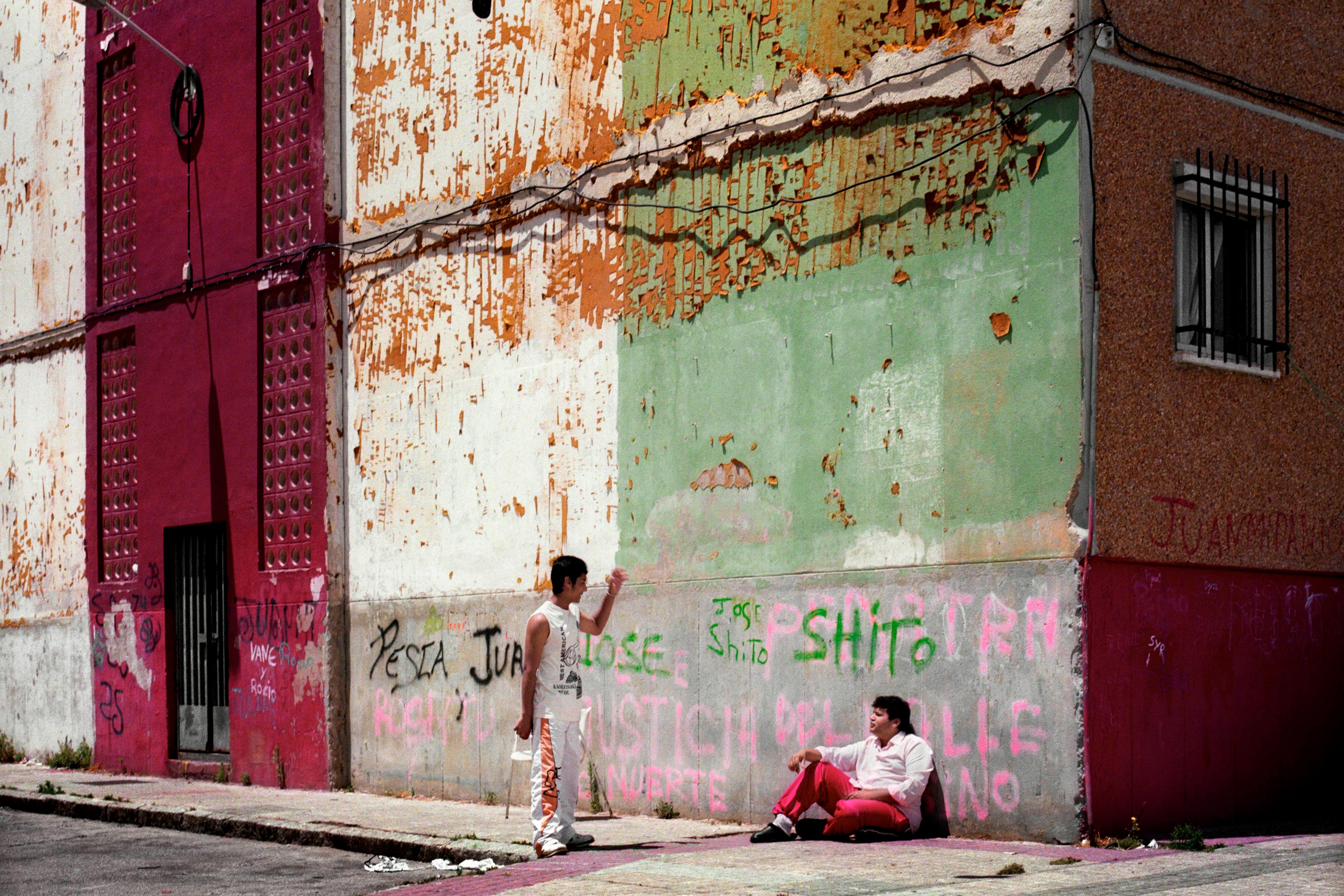Photo of two people in a gritty urban street with peeling painted walls, graffiti and shoes hanging on a wire.