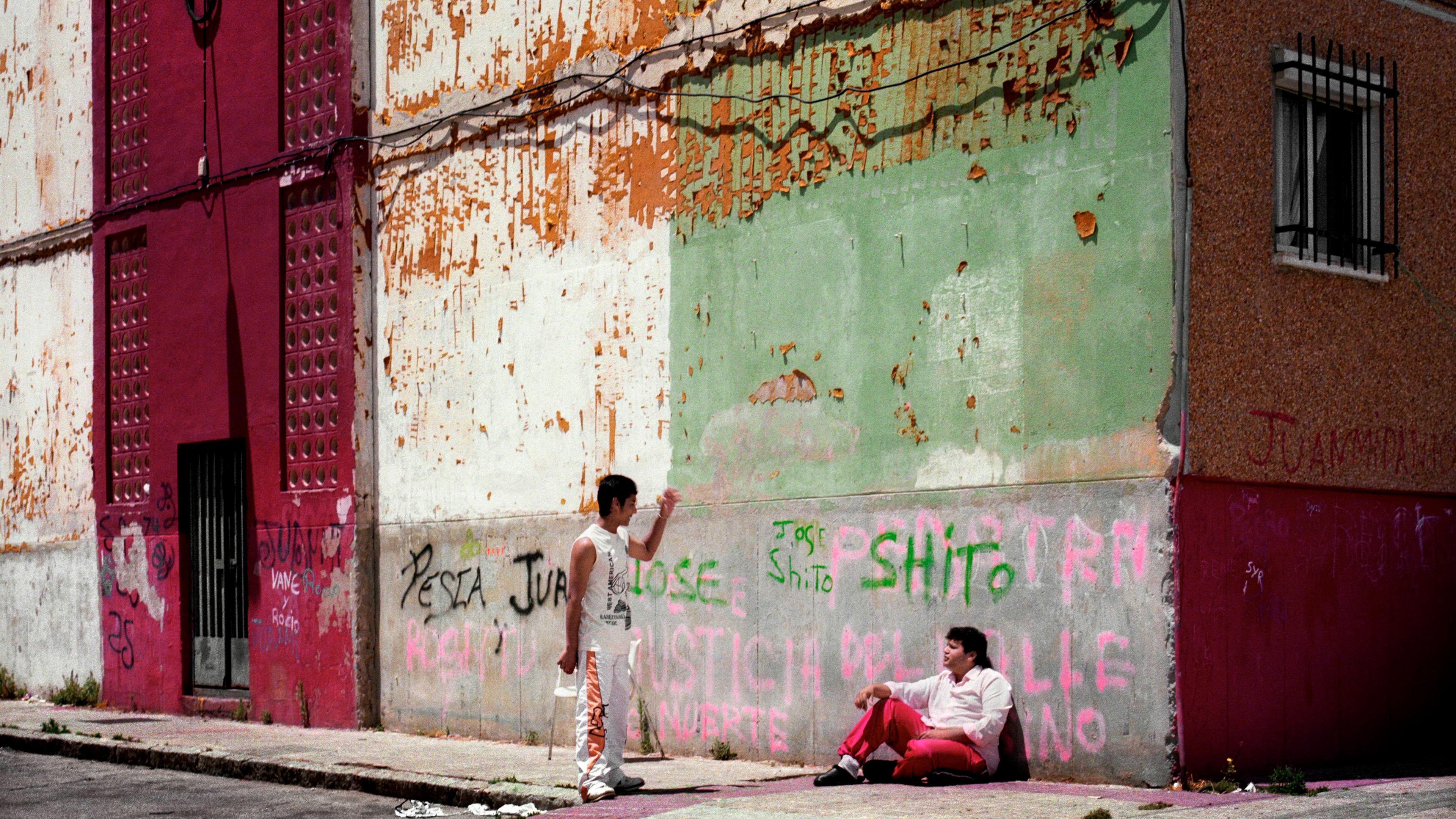 Photo of two people in a gritty urban street with peeling painted walls, graffiti and shoes hanging on a wire.