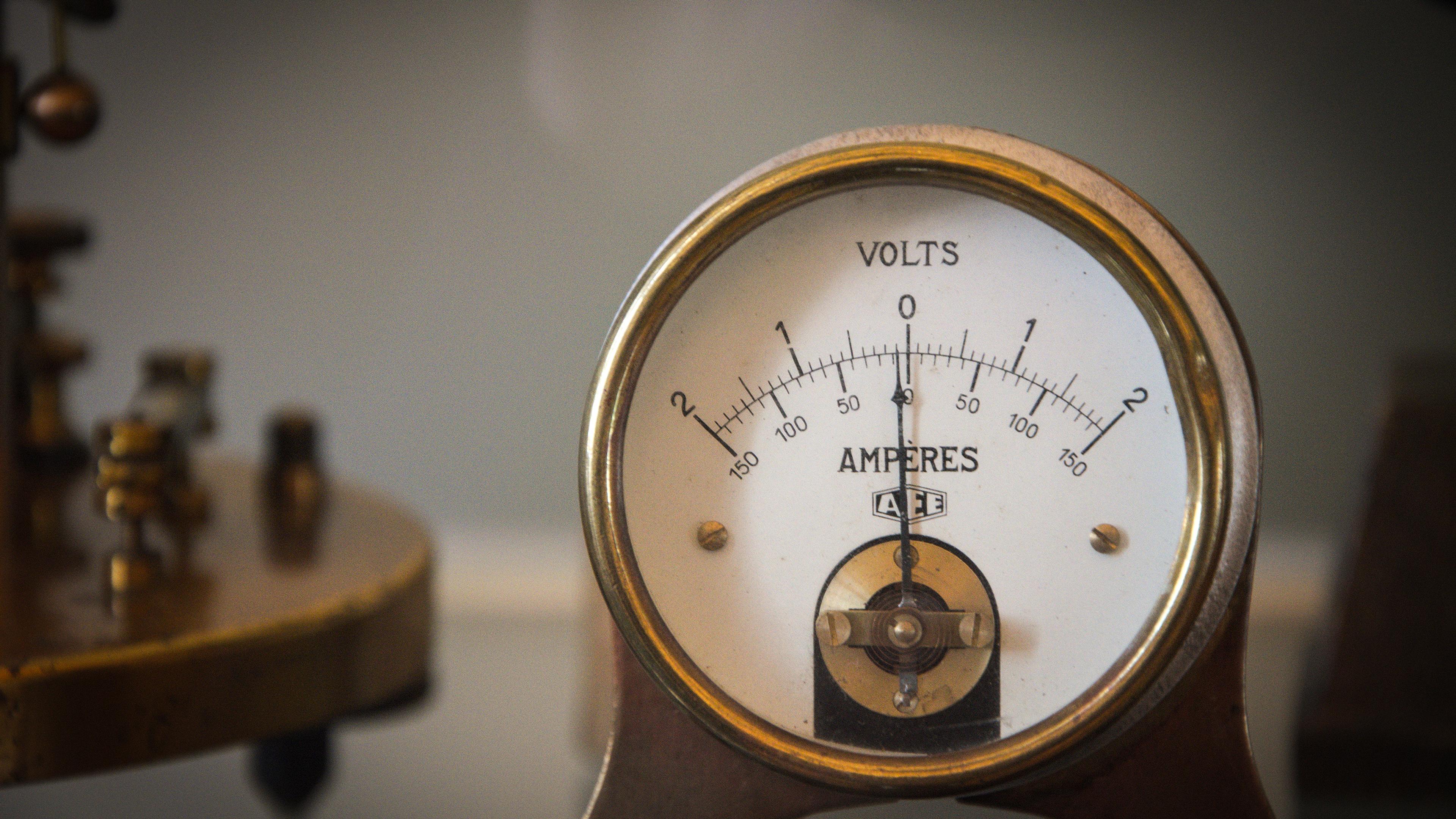 A vintage voltmeter displaying a scale in volts and ampères with a brass base and needle indicator.