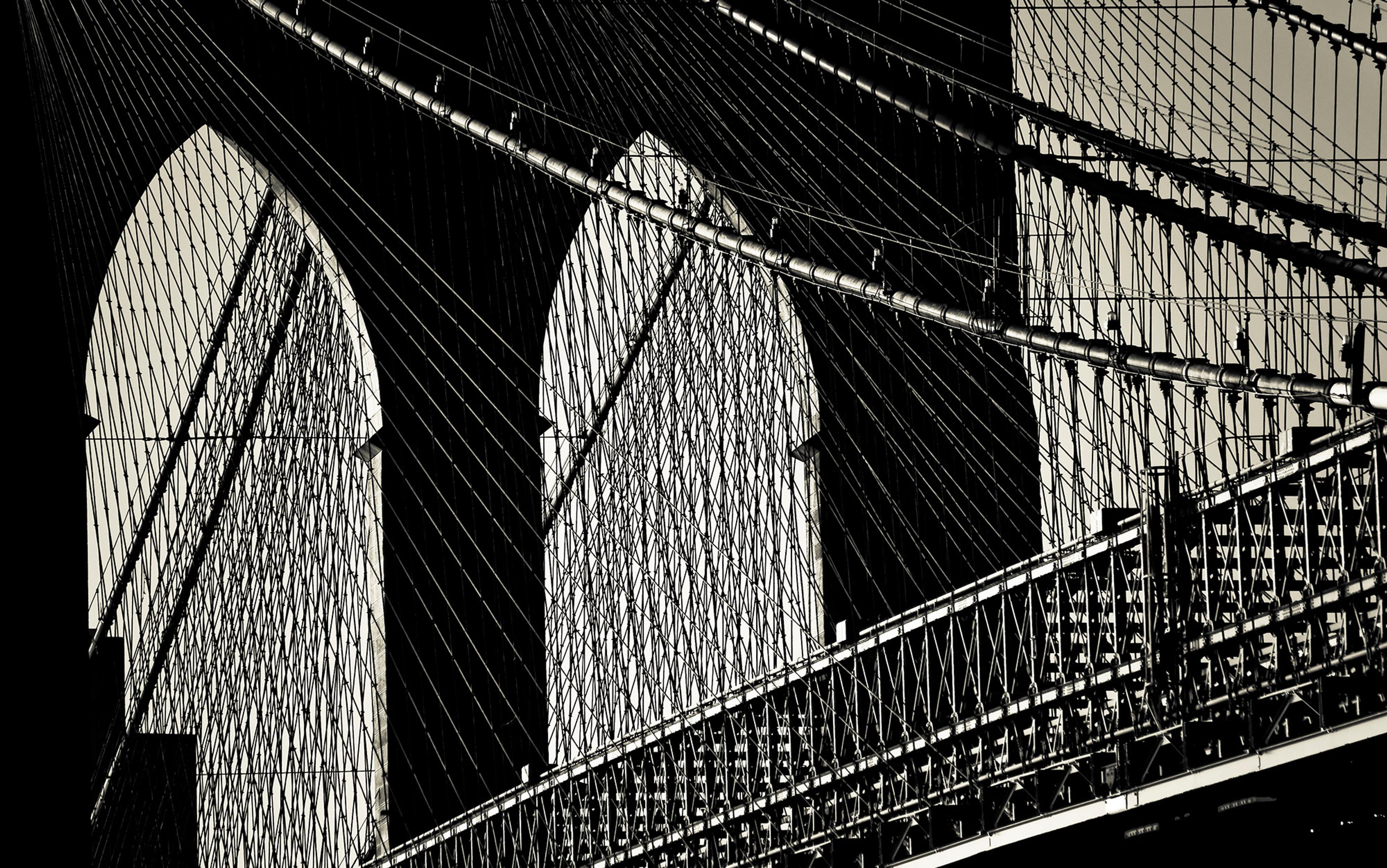 Black and white photo of a suspension bridge with intricate cables and arched supports, viewed from a close-up angle.