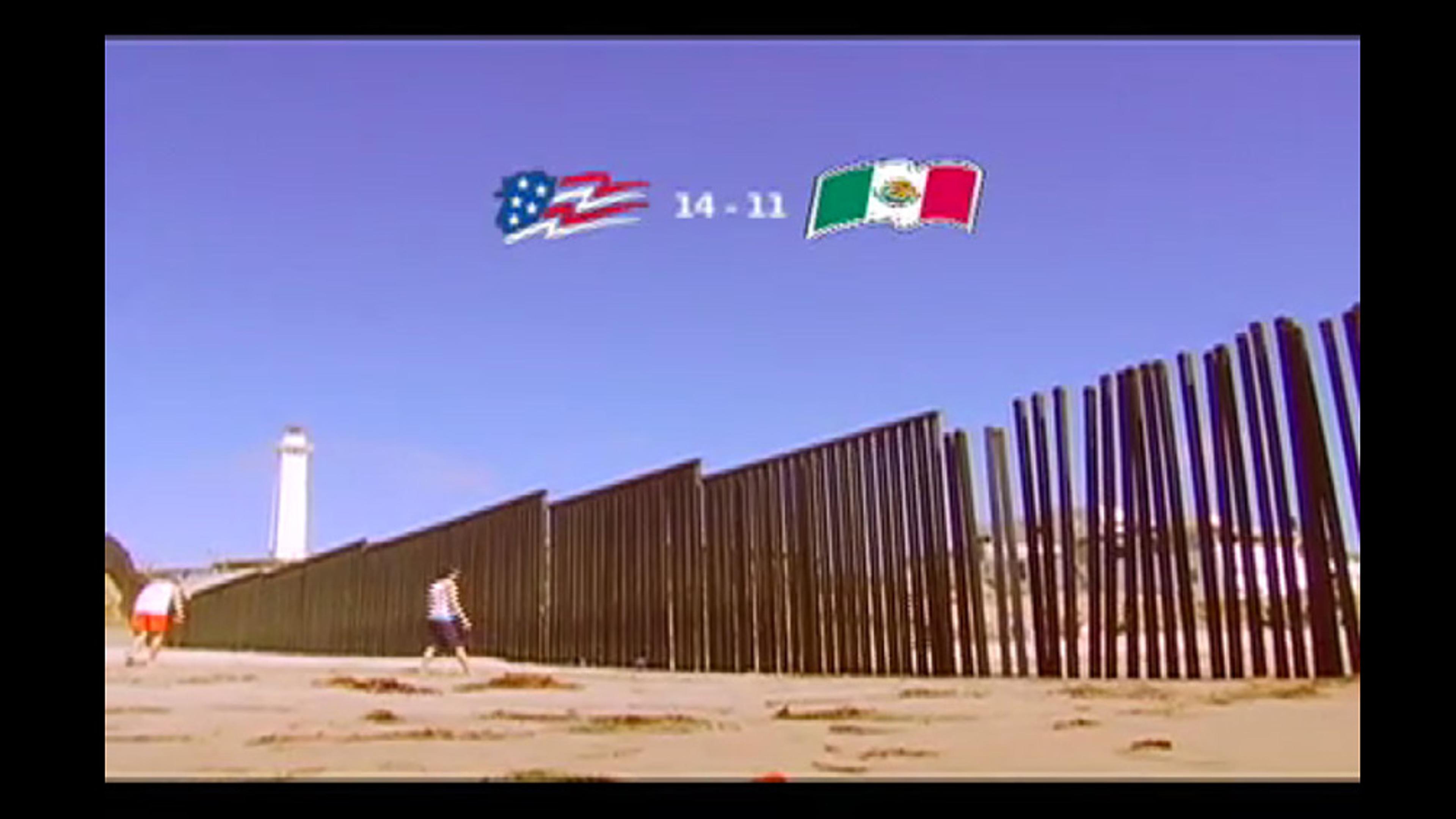 A beach with a metal fence stretching towards a lighthouse under a blue sky, featuring USA and Mexican flags with scores.