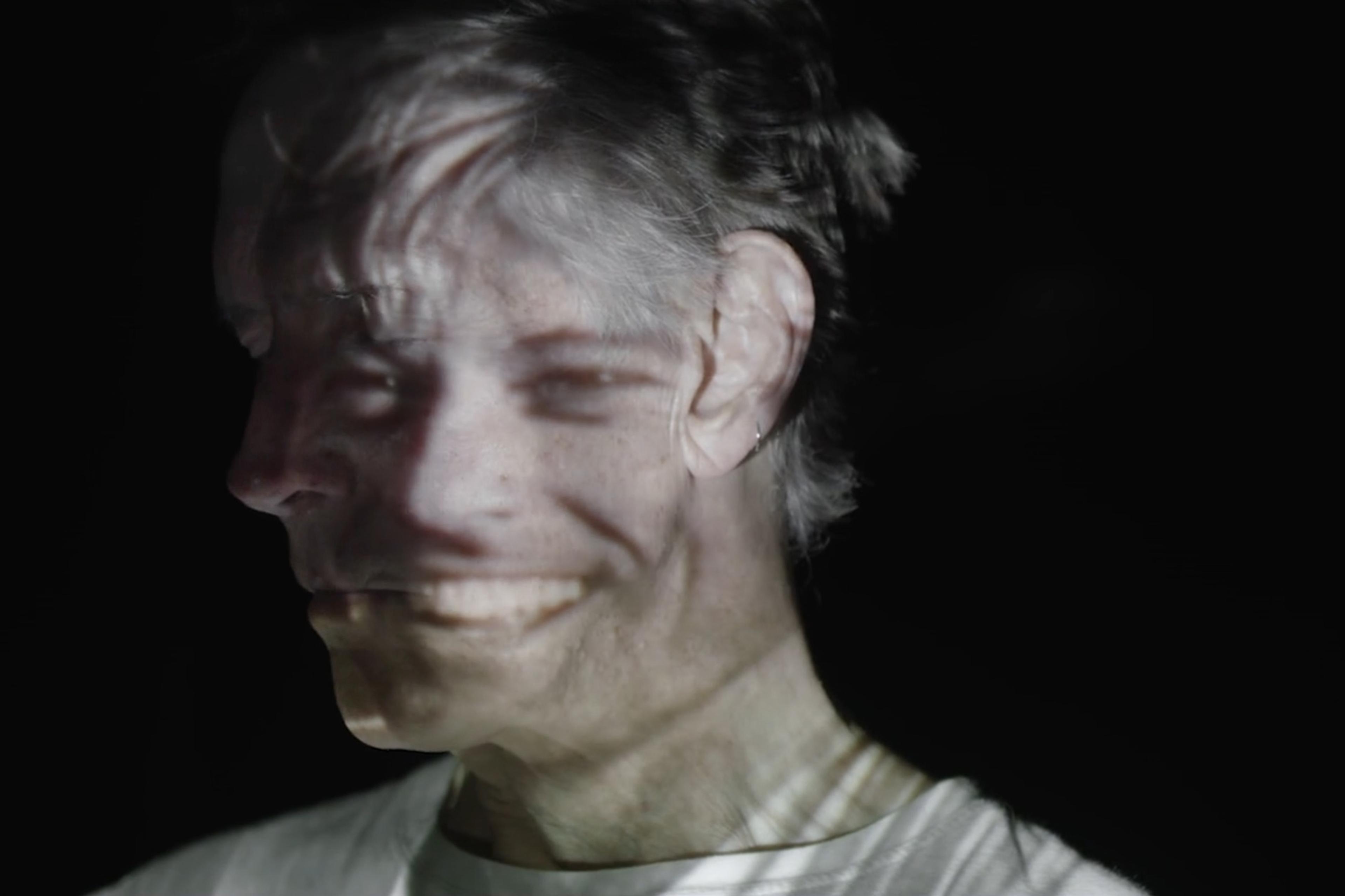 An image of a man’s face with a photograph of a smiling face projected onto it, creating a surreal, double-exposure effect.