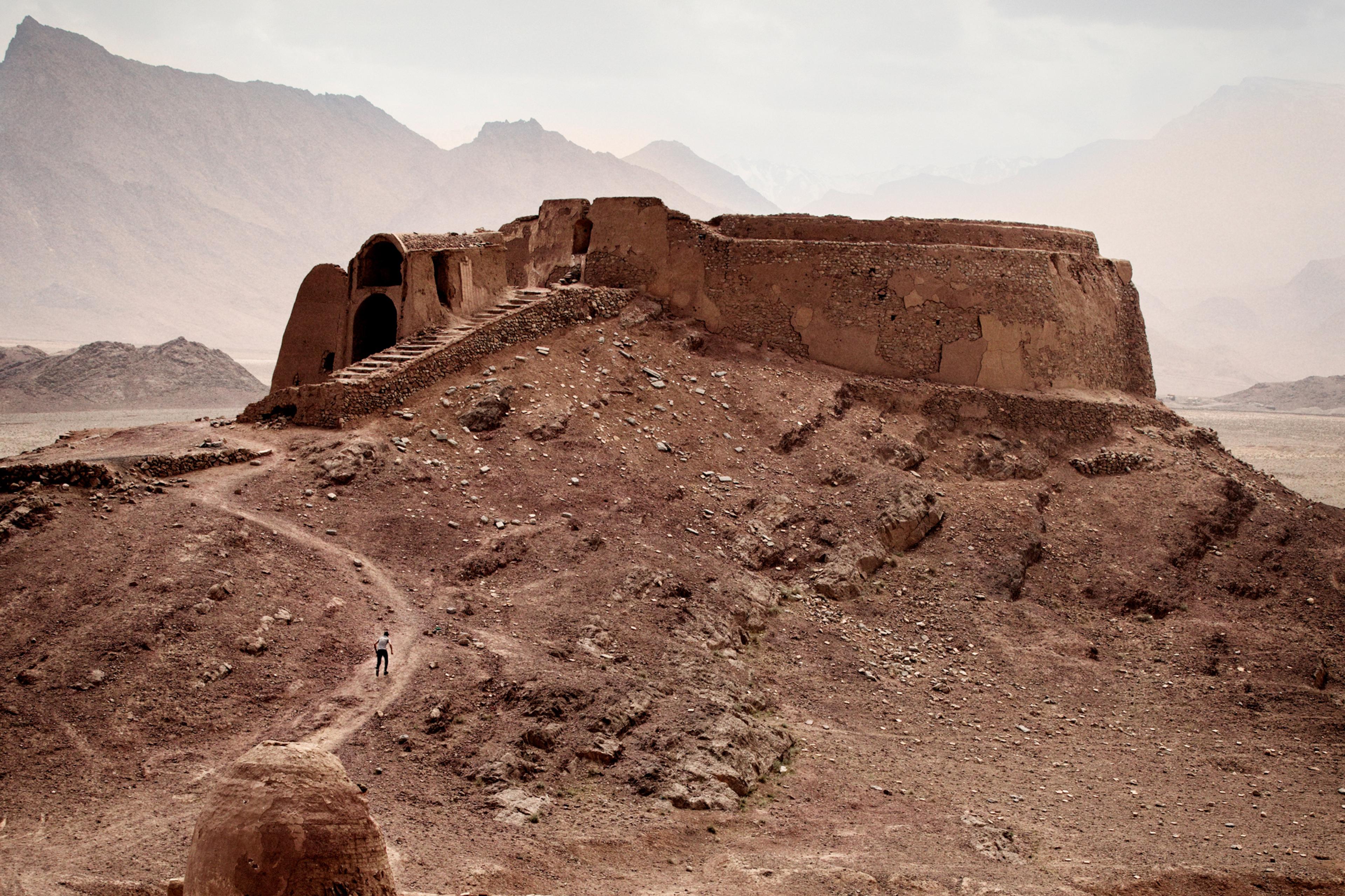 Photo of ancient ruins on a rocky hill with a cloudy sky and distant mountains in the background.