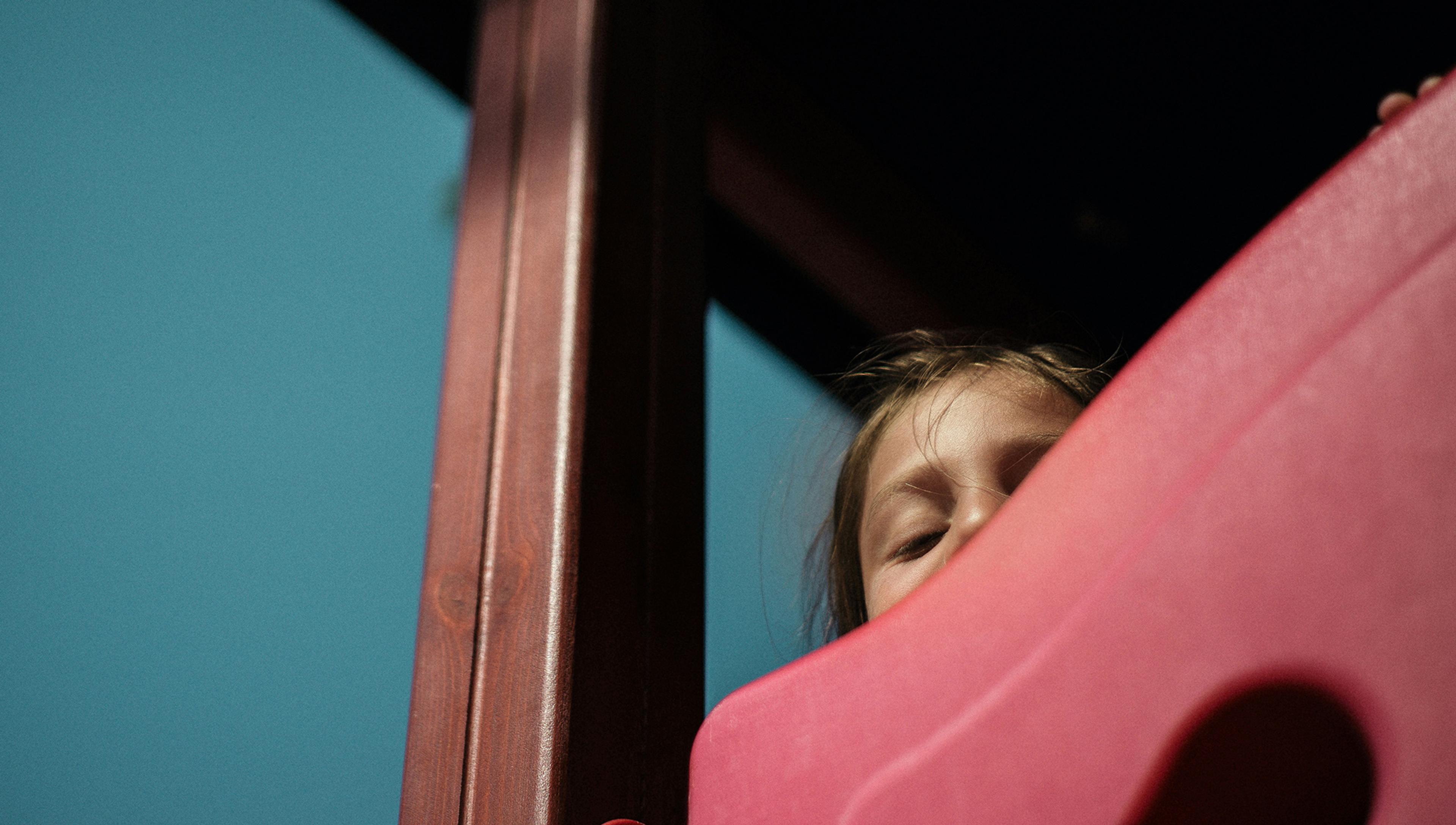 a frightened child whose face is partially obscured peers down from by a play area structure