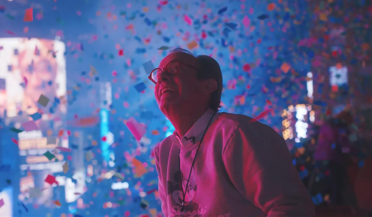 A person in glasses smiles amid colourful confetti in the air, with blurry, illuminated urban background and celebratory atmosphere.