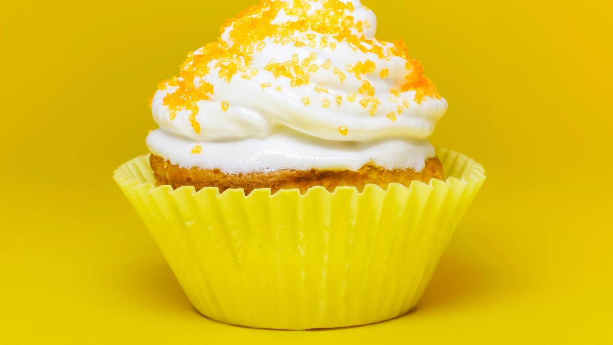 Photo of a cupcake with white icing and orange sprinkles in a yellow wrapper against a bright yellow background.