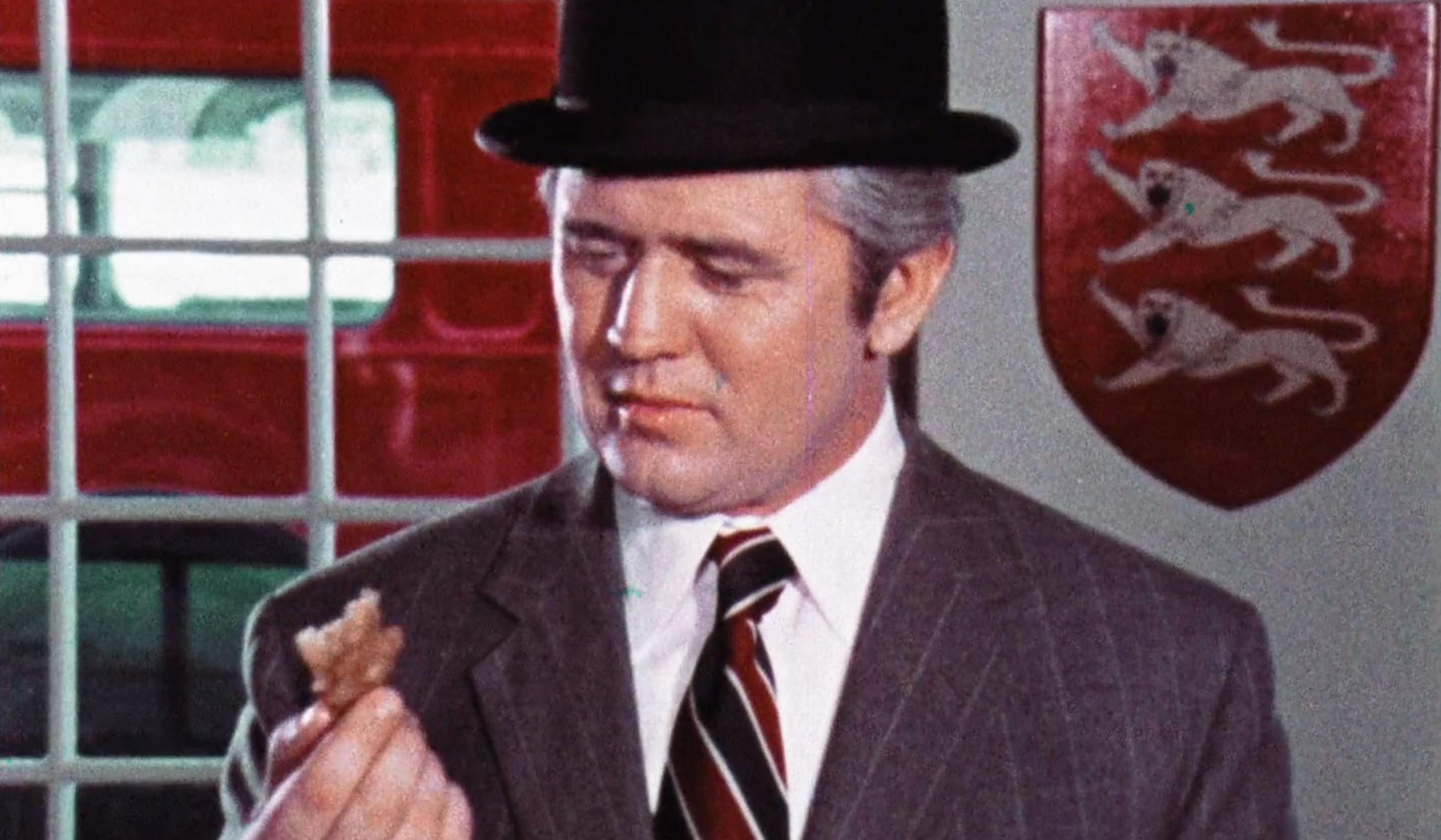 Man in a suit and bowler hat inspecting an item, with a red bus and a shield with three lions in the background.