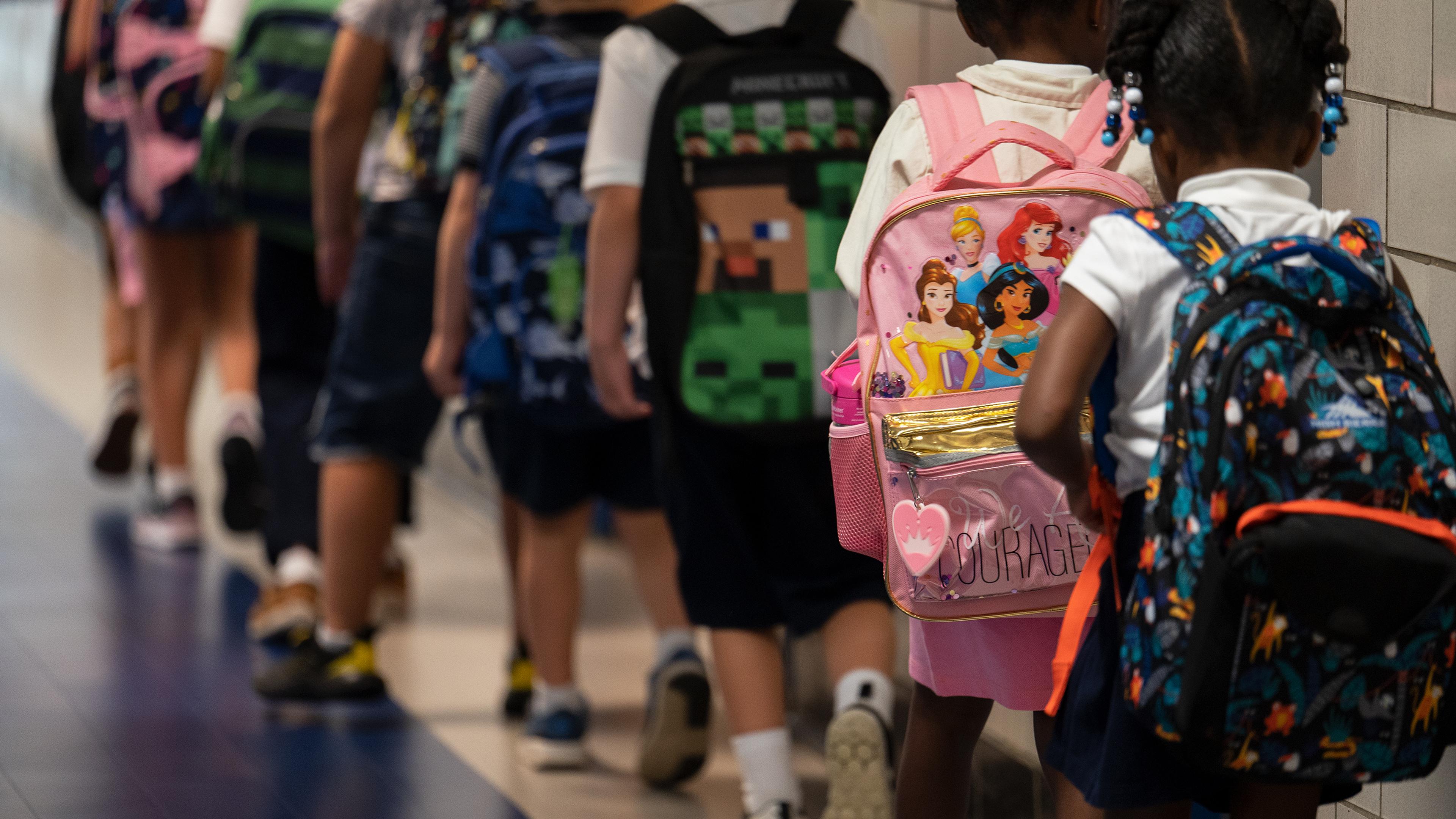 Photo of children with backpacks walking in a school corridor.