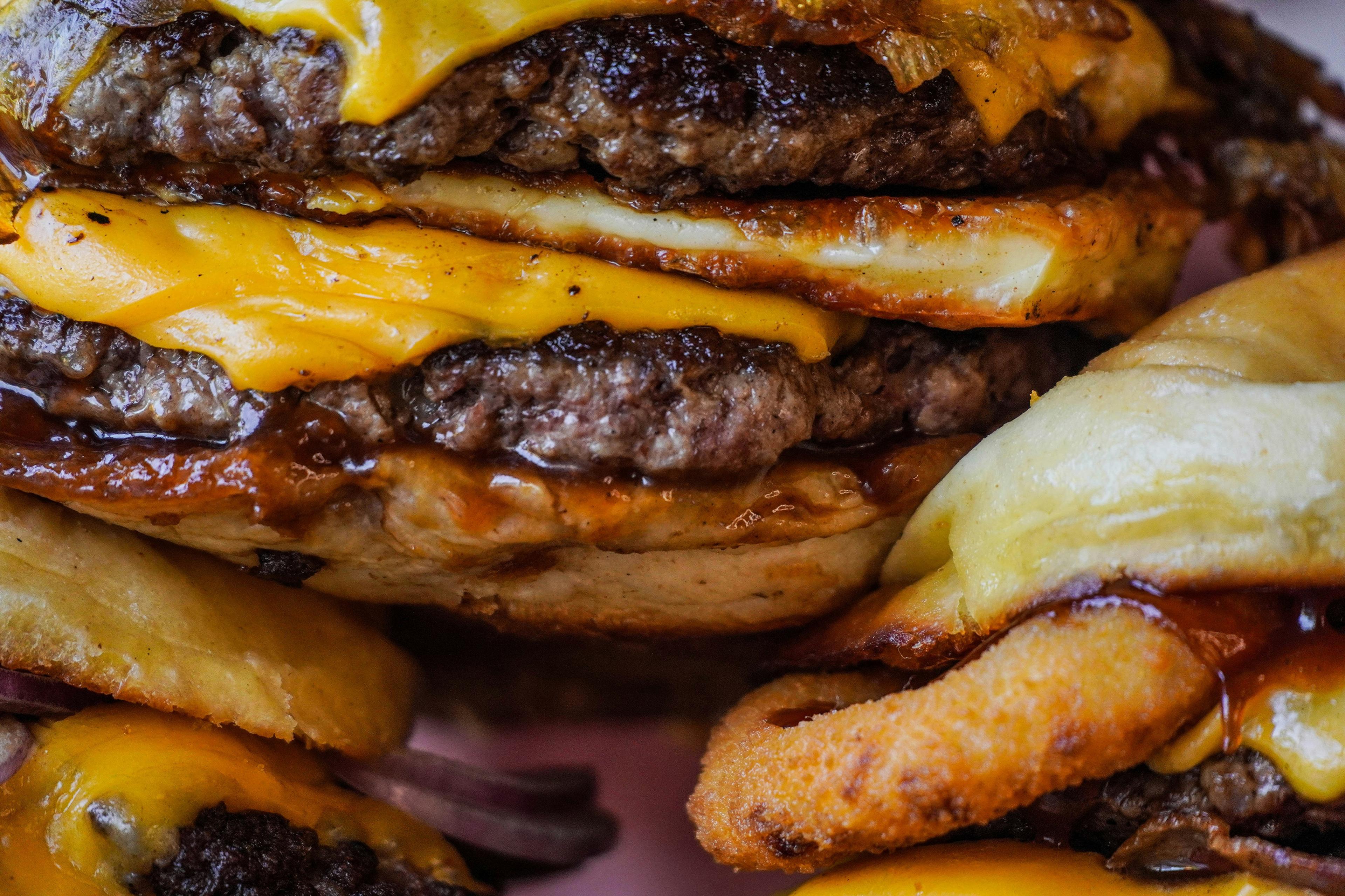 A close-up view of a cheeseburger with multiple beef patties, melted cheese and crispy onion rings.