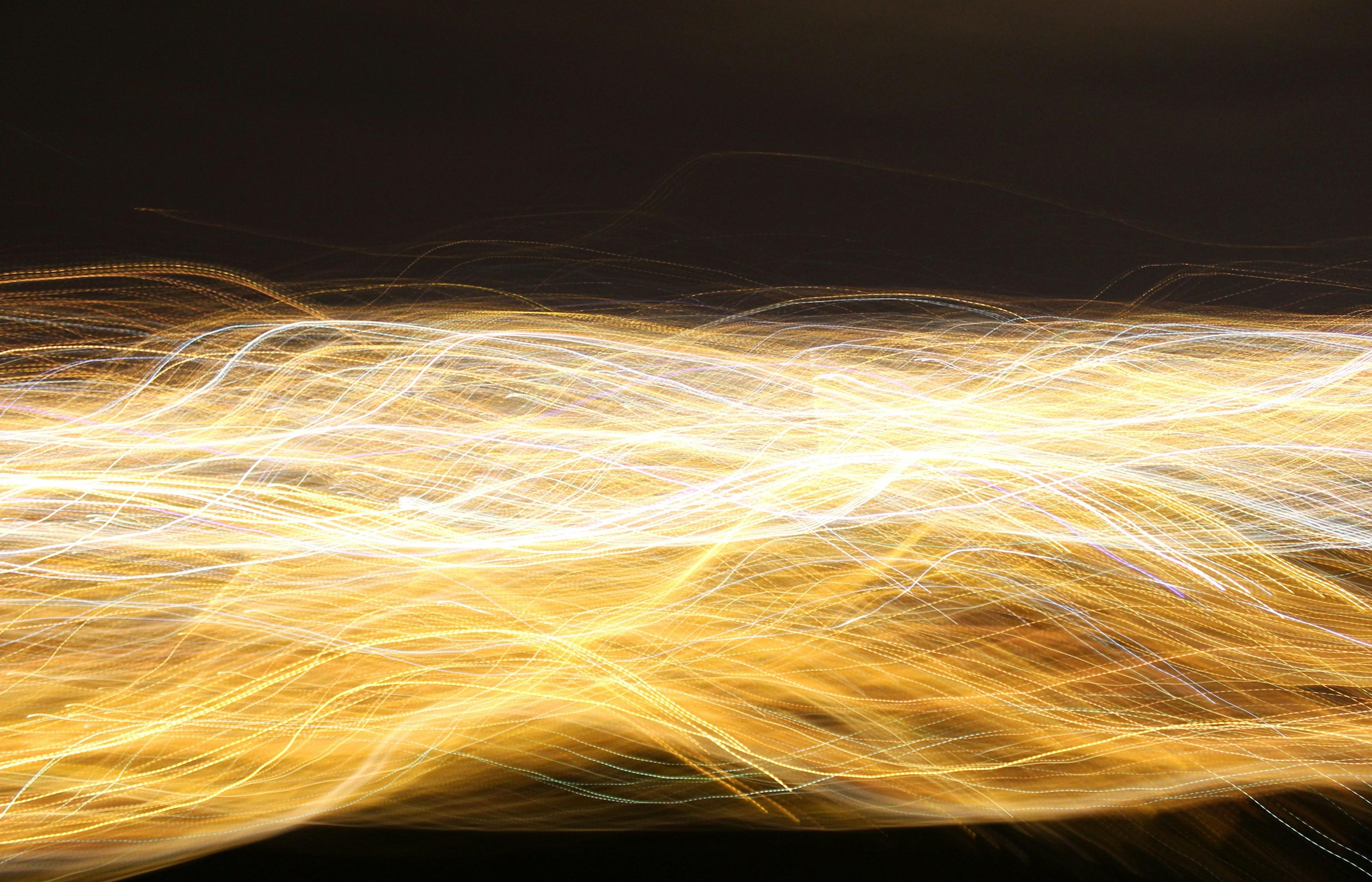 Photo of abstract light trails in yellow and white on a dark background, creating a swirling, dynamic pattern.