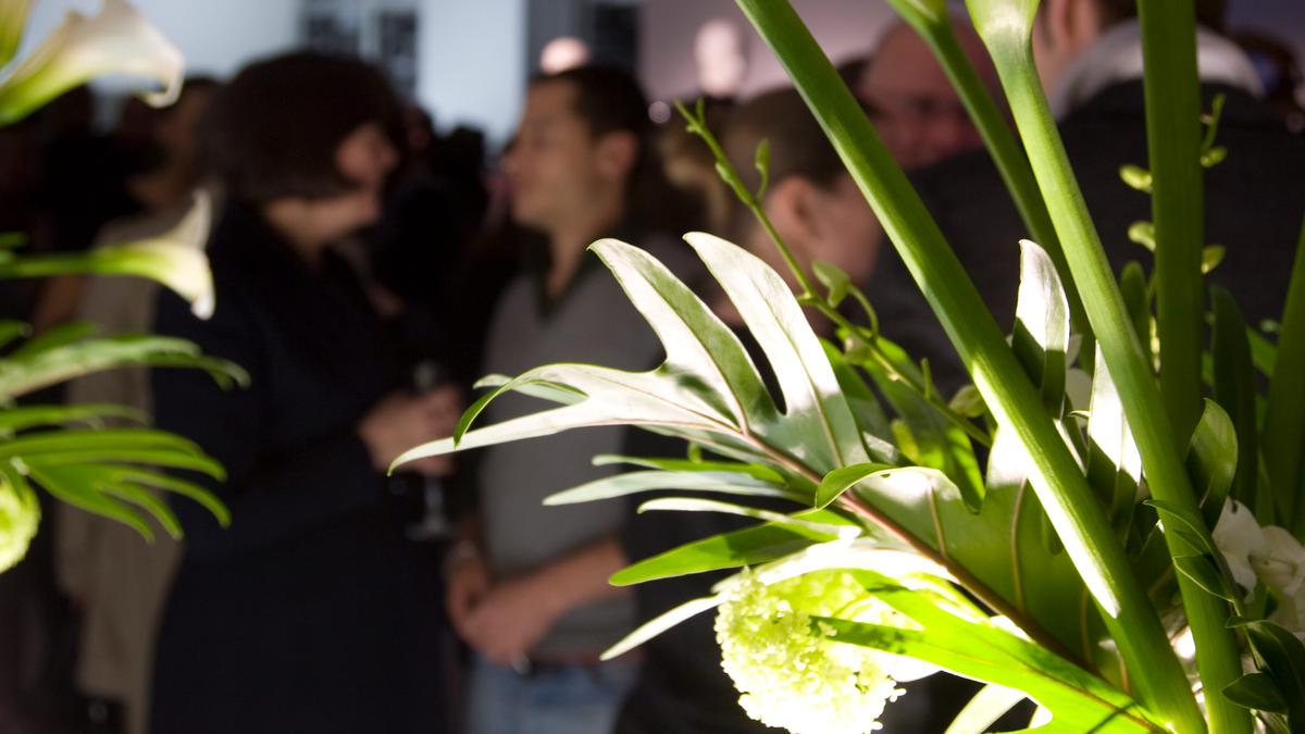 Photo of a crowded event with out-of-focus people in the background and sharply focused green and white flowers in the foreground.