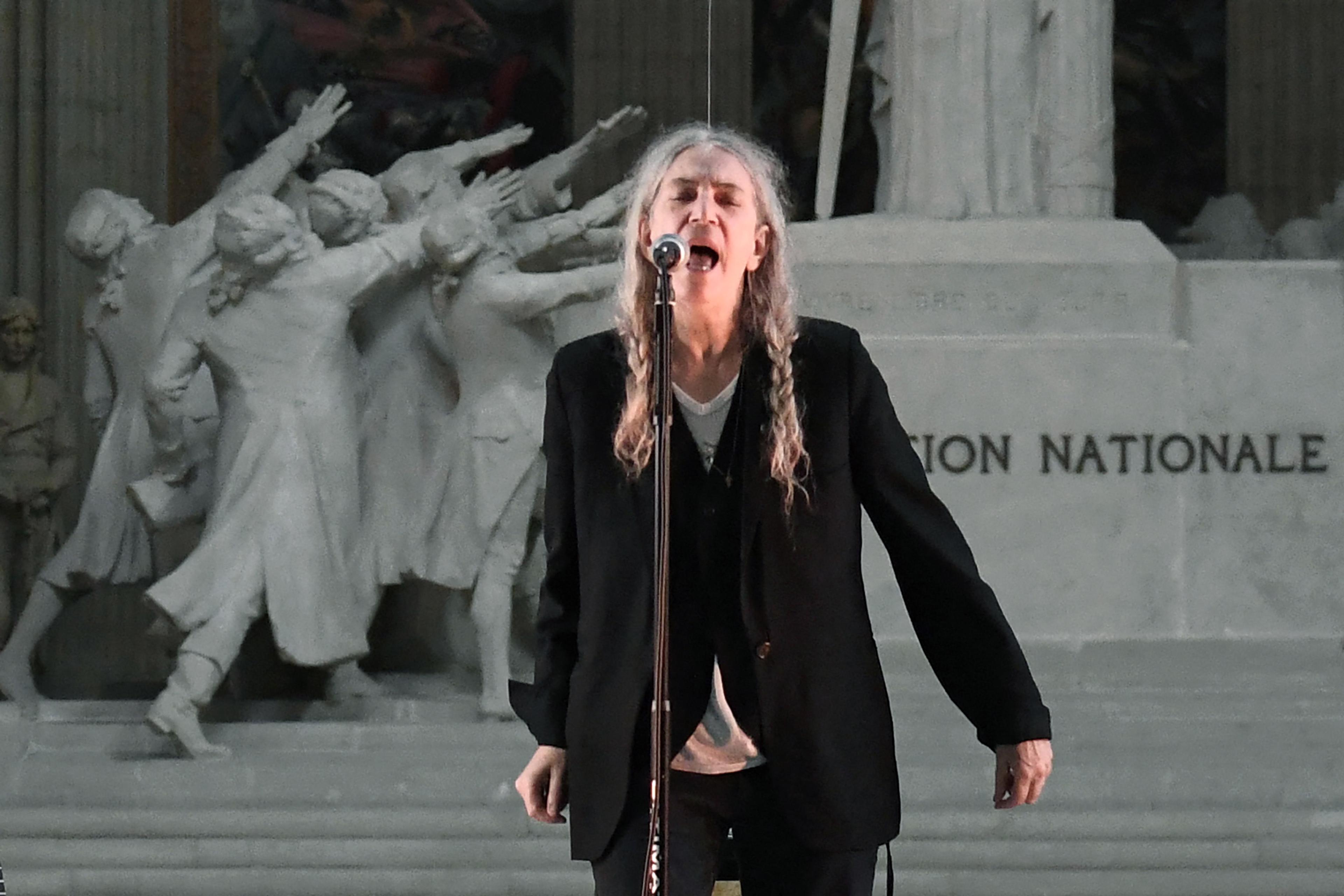 Photo of a person singing passionately into a microphone with a historic sculpture in the background.