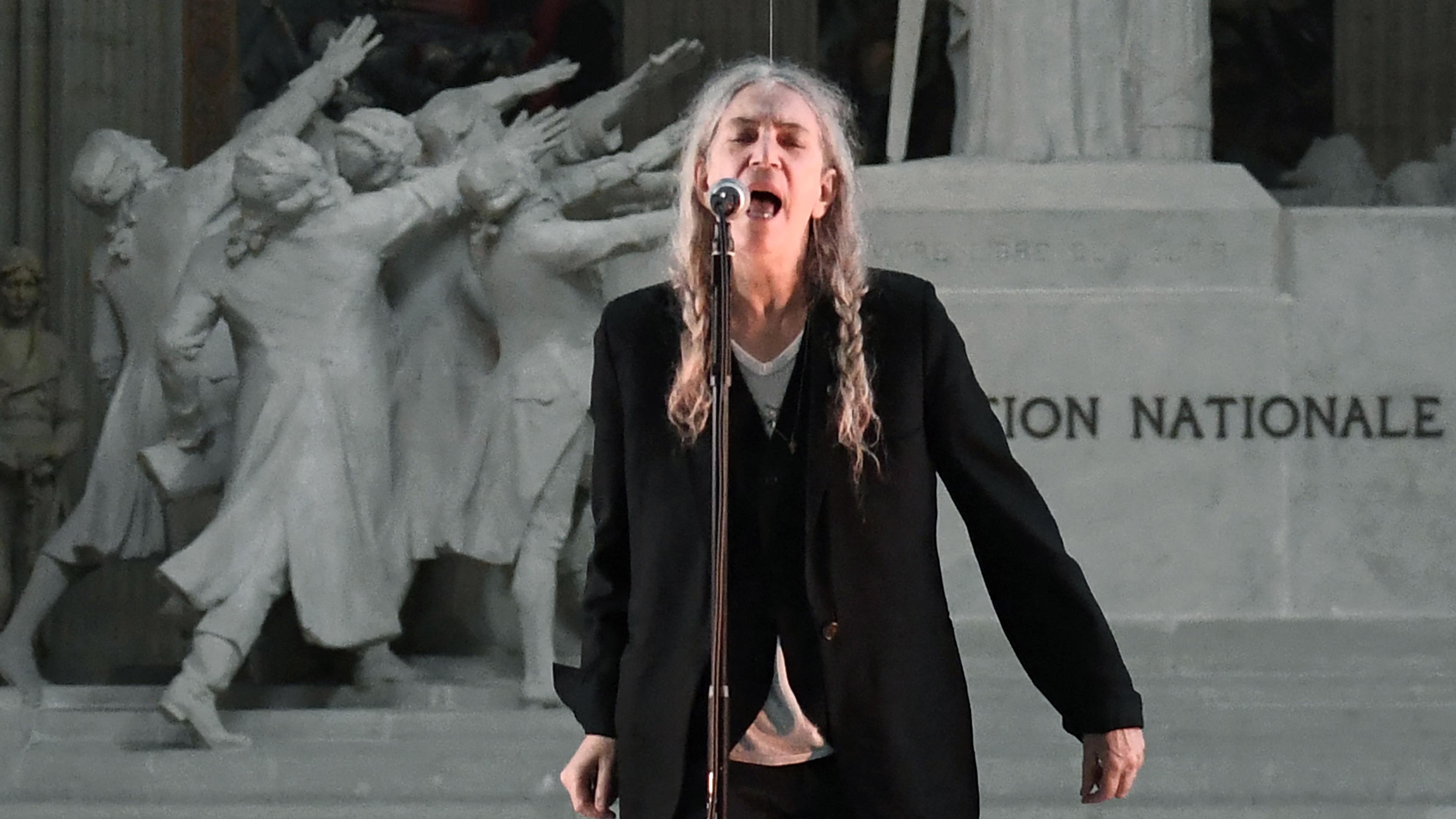 Photo of a person singing passionately into a microphone with a historic sculpture in the background.