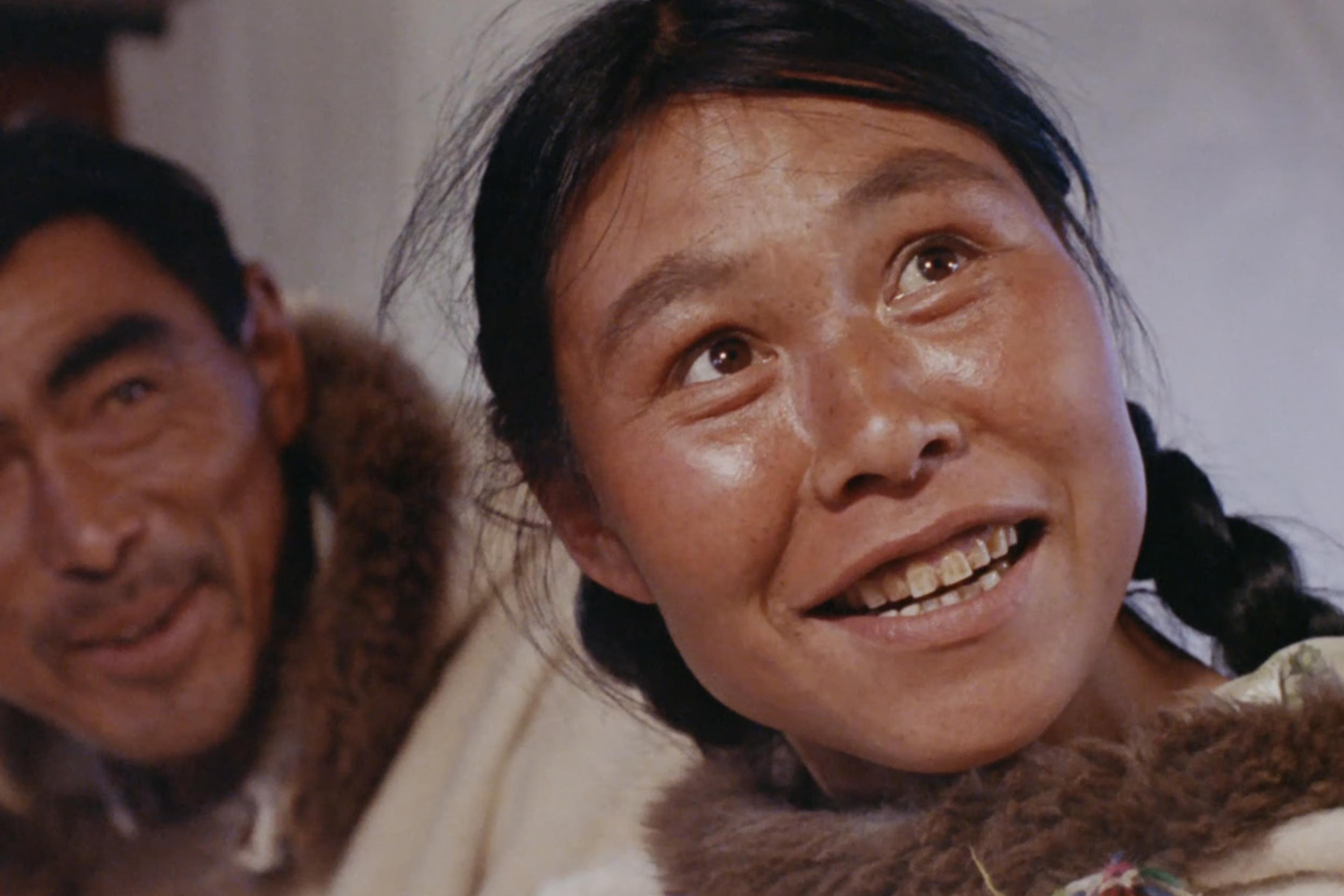 A film still showing the Inuit artist Kenojuak Ashevak and her husband Johnniebo in fur-trimmed clothing, smiling and looking off camera.