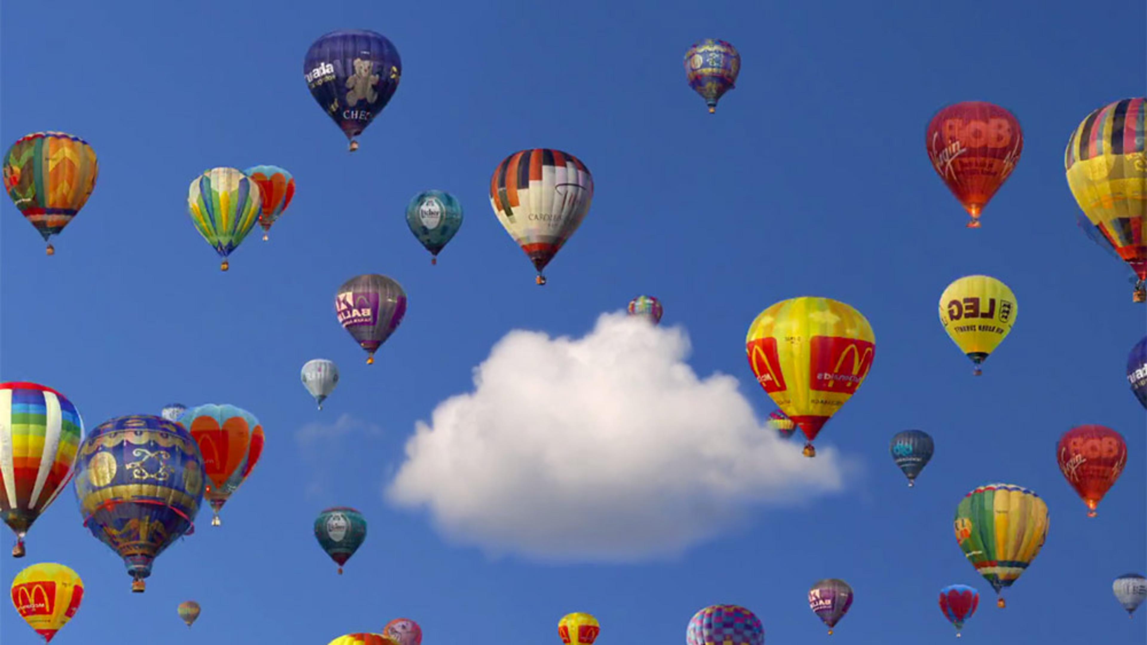 Colourful hot air balloons floating against a blue sky with a single white cloud in the centre.
