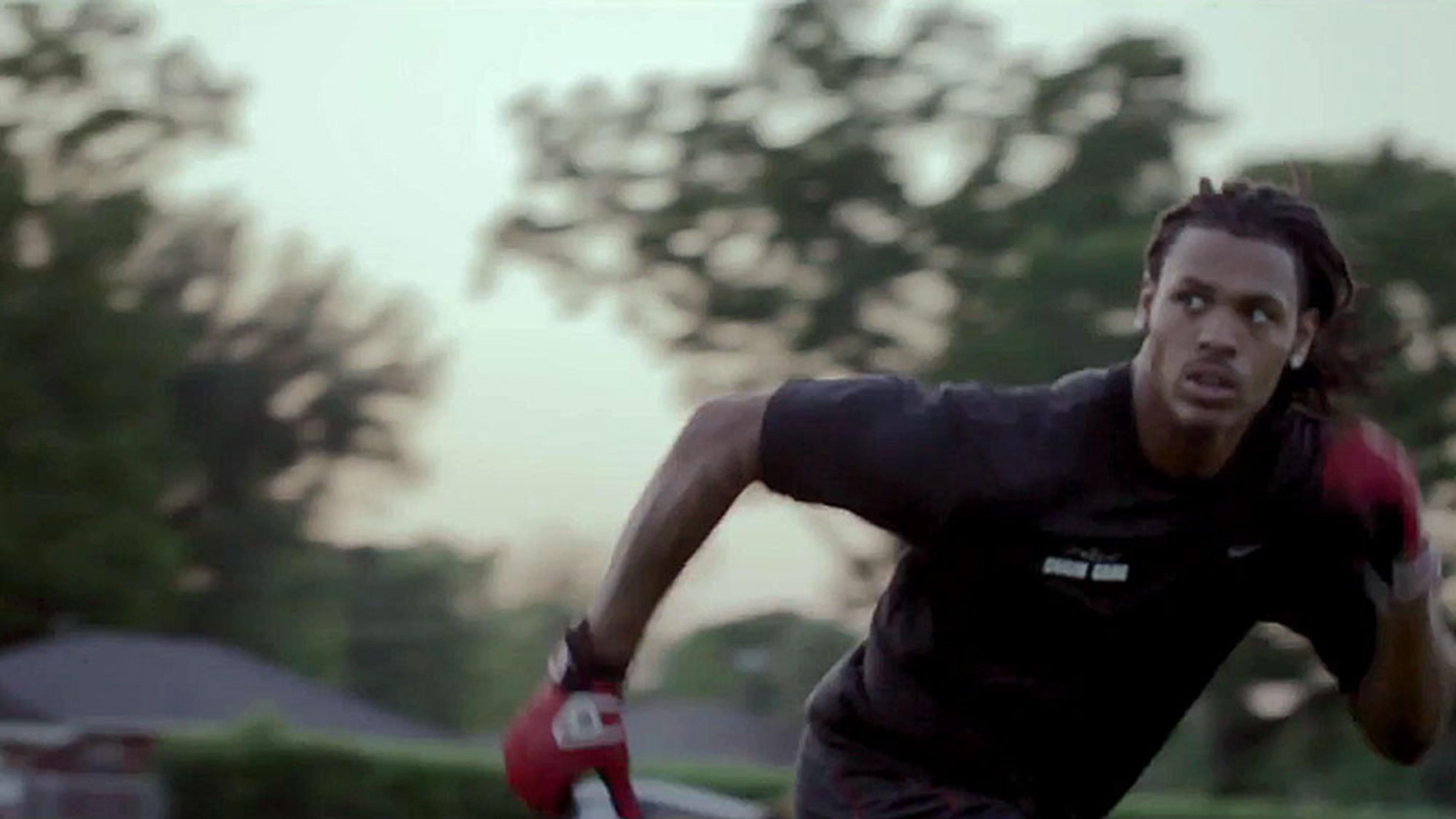 A Black man in a black shirt and red gloves, running outdoors with trees in the background at dusk.