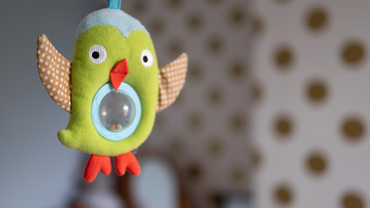 A colourful plush owl toy with polka-dot wings hanging indoors against a polka-dotted wall background.
