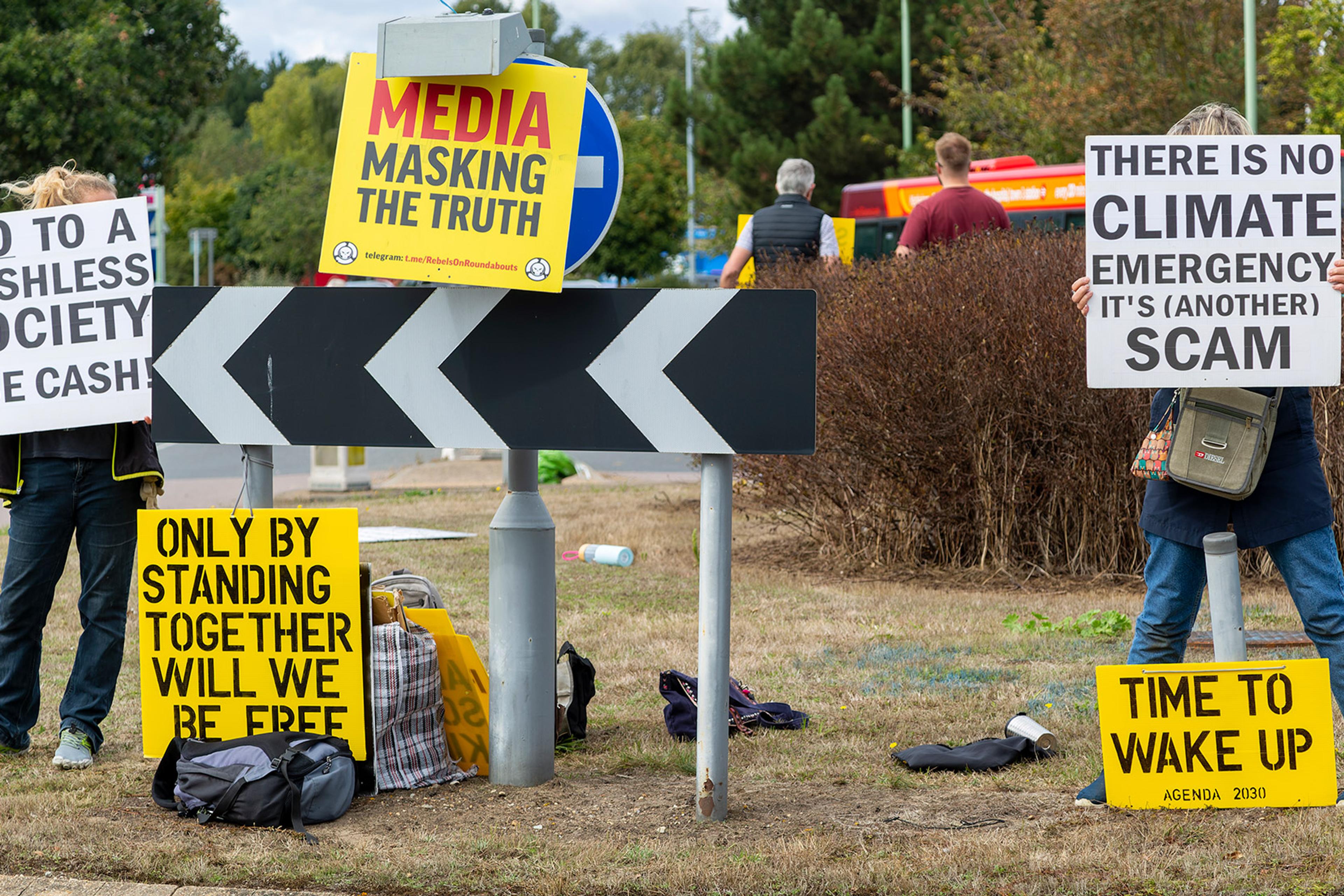 Protesters holding signs against cashless society, media and climate emergency. Signs include “ONLY BY STANDING TOGETHER WILL WE BE FREE” and “TIME TO WAKE UP”.