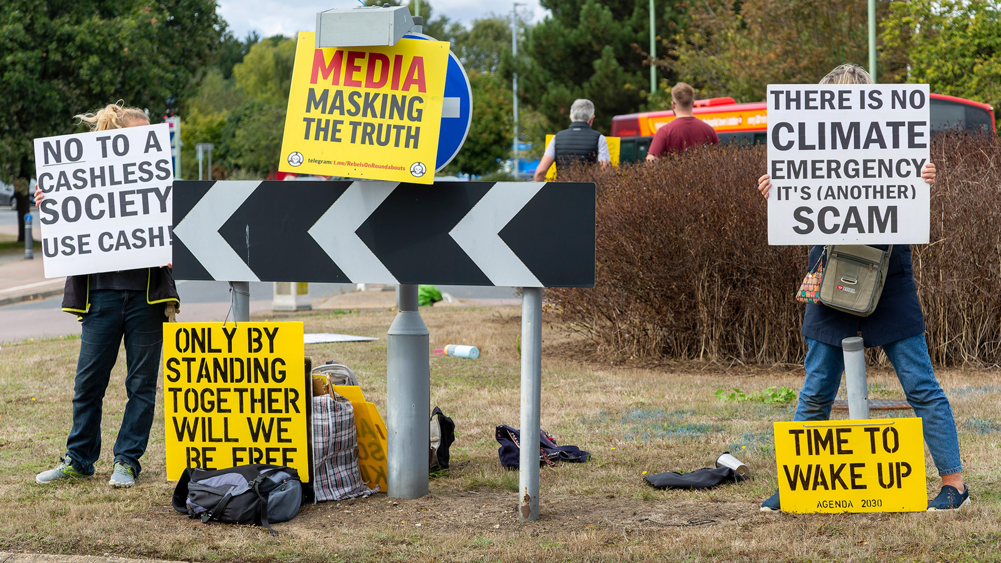 Protesters holding signs against cashless society, media and climate emergency. Signs include “ONLY BY STANDING TOGETHER WILL WE BE FREE” and “TIME TO WAKE UP”.