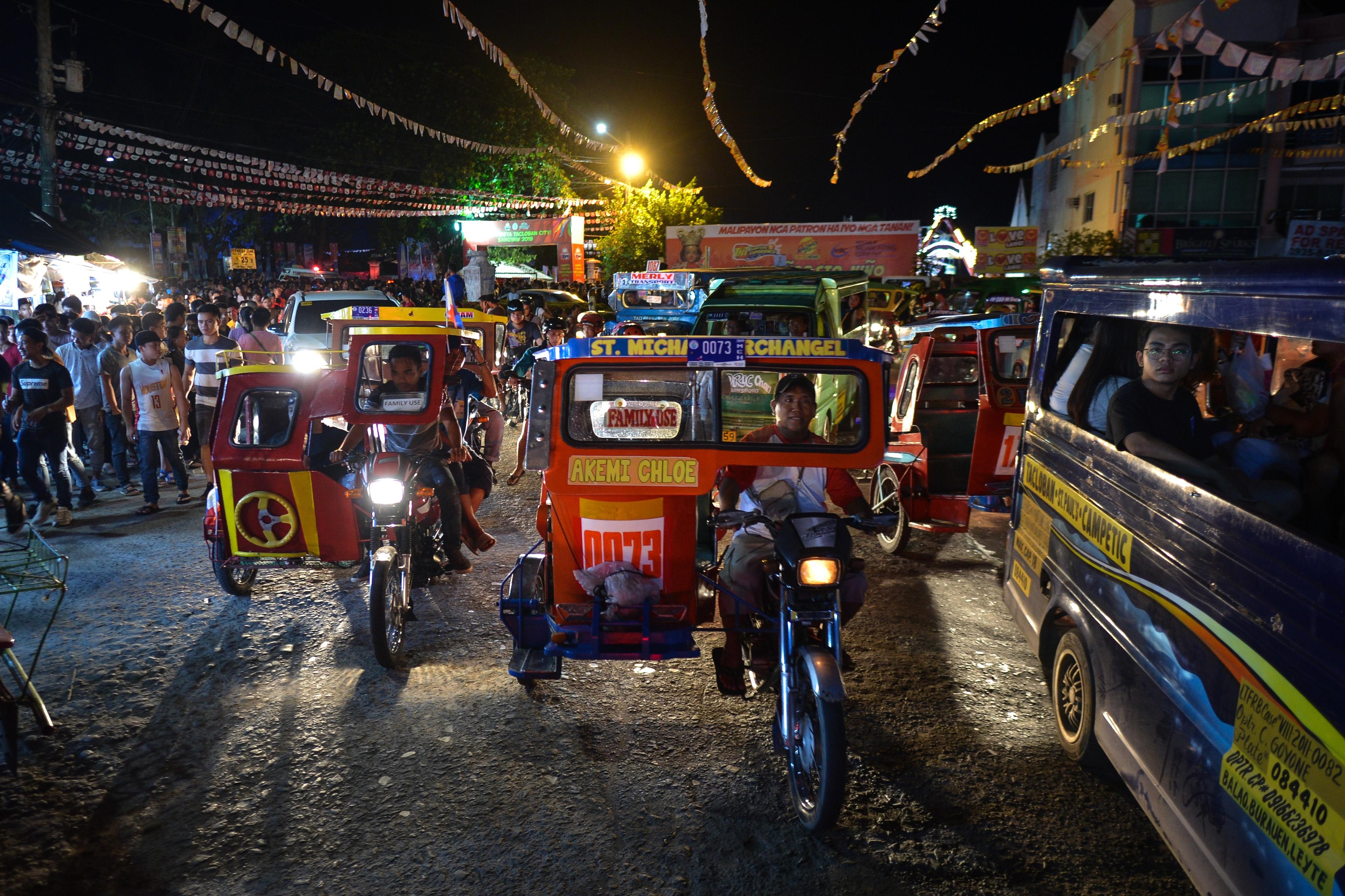 Photo of a bustling night market with colourful tricycles, a crowded street and illuminated stalls in the background.