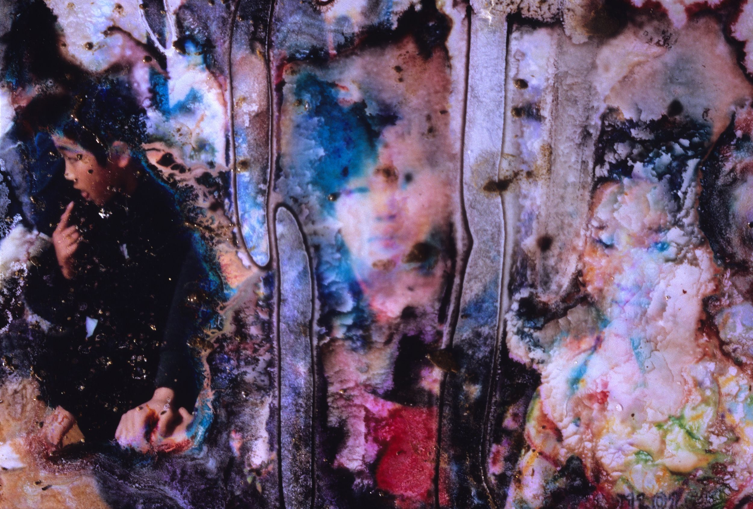 A damaged photograph showing a blur of vivid colours and textures, featuring a partially visible figure of a child on the left side.