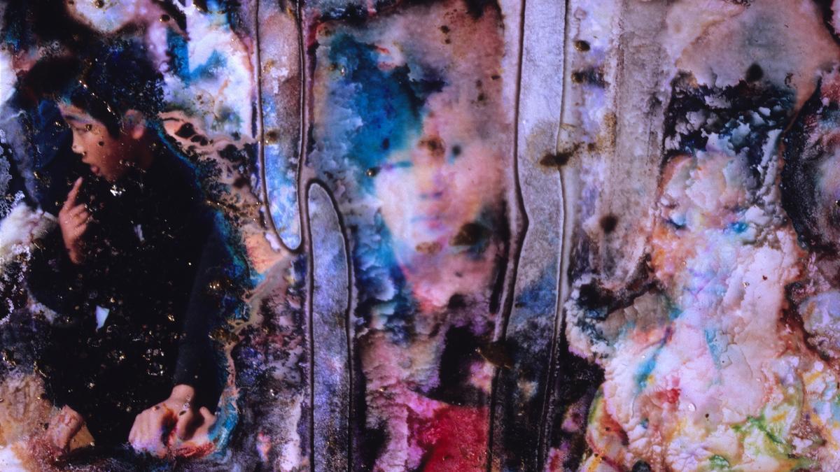 A damaged photograph showing a blur of vivid colours and textures, featuring a partially visible figure of a child on the left side.